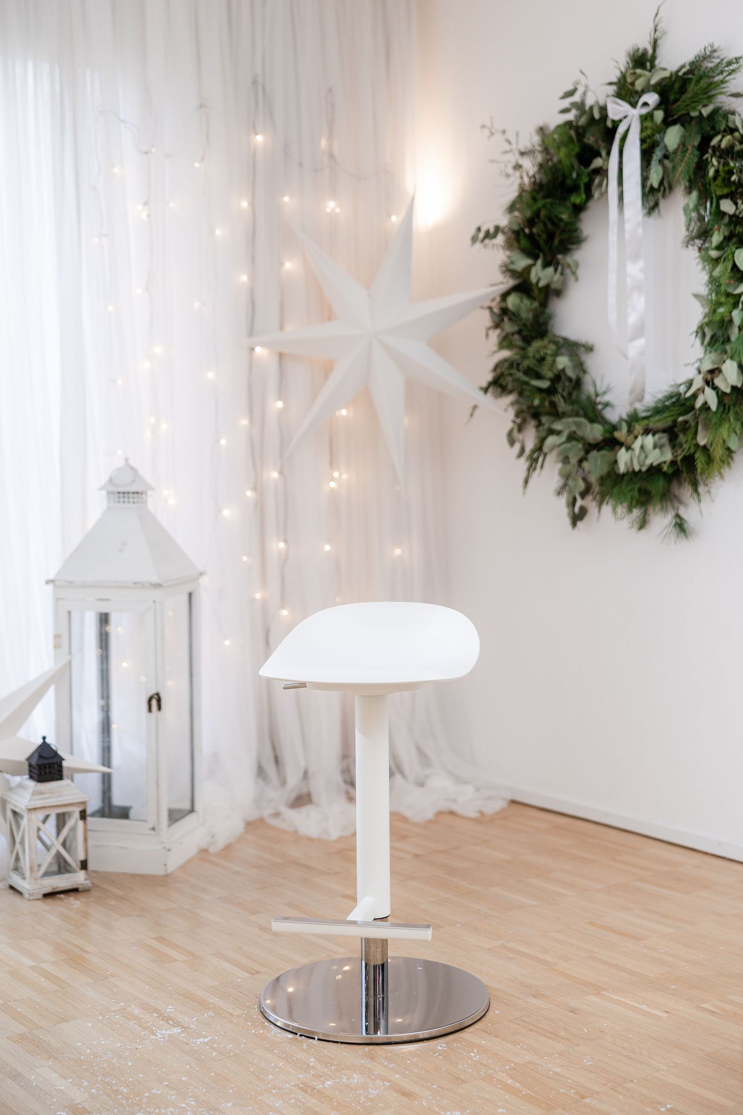 Modern white bar stool against white wall with holiday decor featuring lanterns, twinkle lights and evergreen wreath.