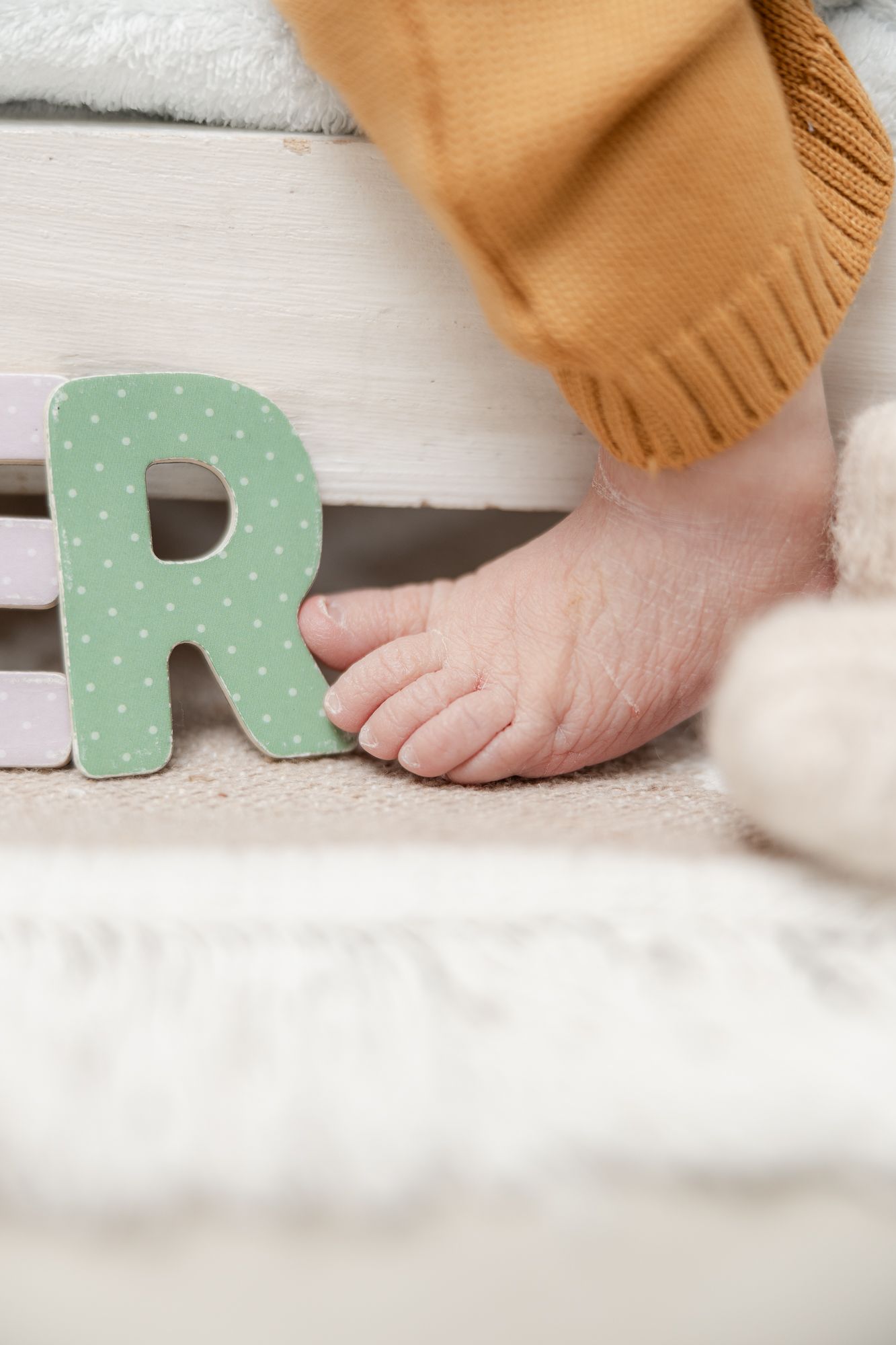 Bare feet and a mint green polka dot letter R decoration on a soft white carpet or rug surface.