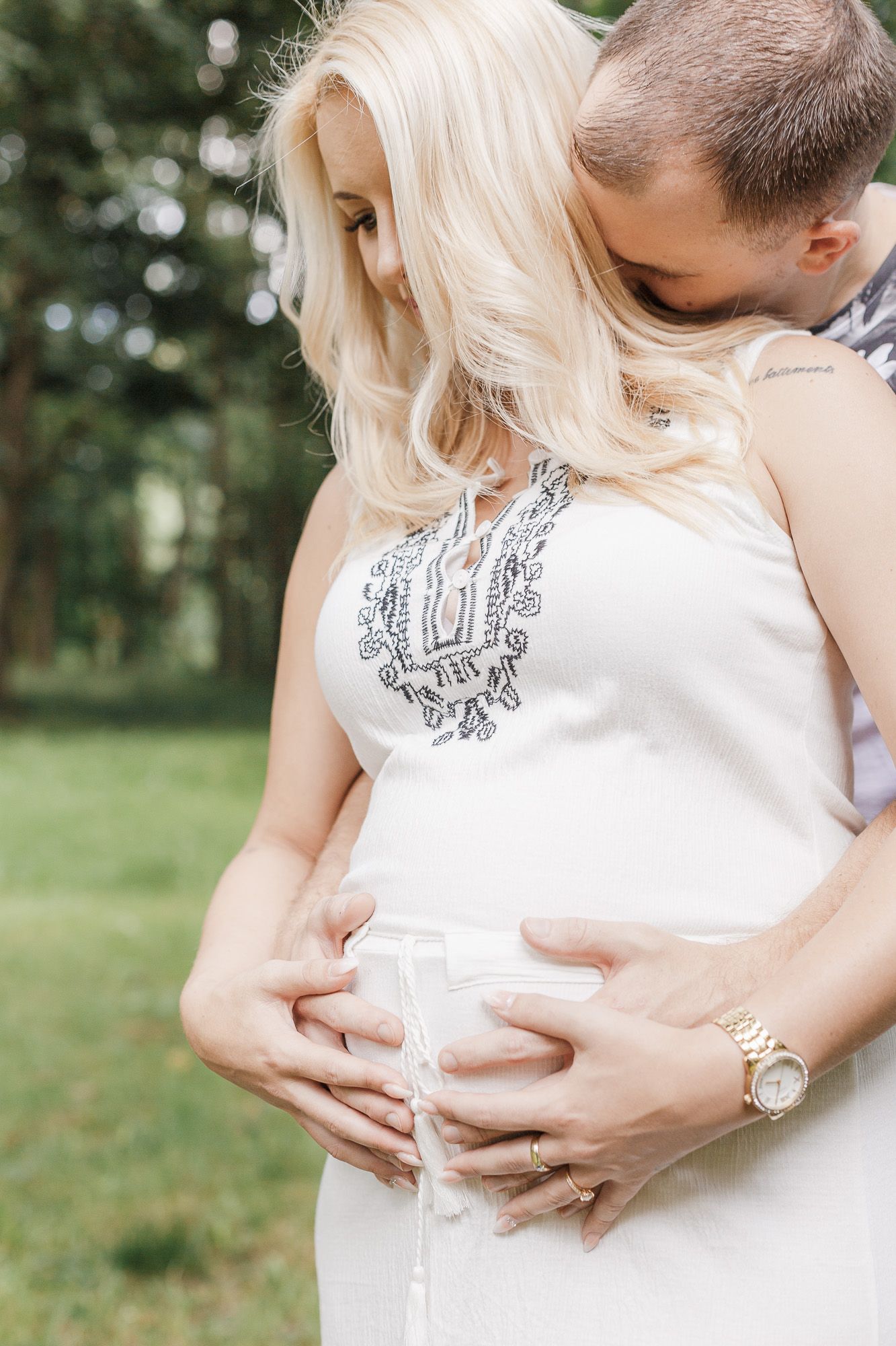 Close-up maternity photos showing hands cradling a pregnant belly in a white dress against an outdoor background - Babybauch Fotograf Aargau