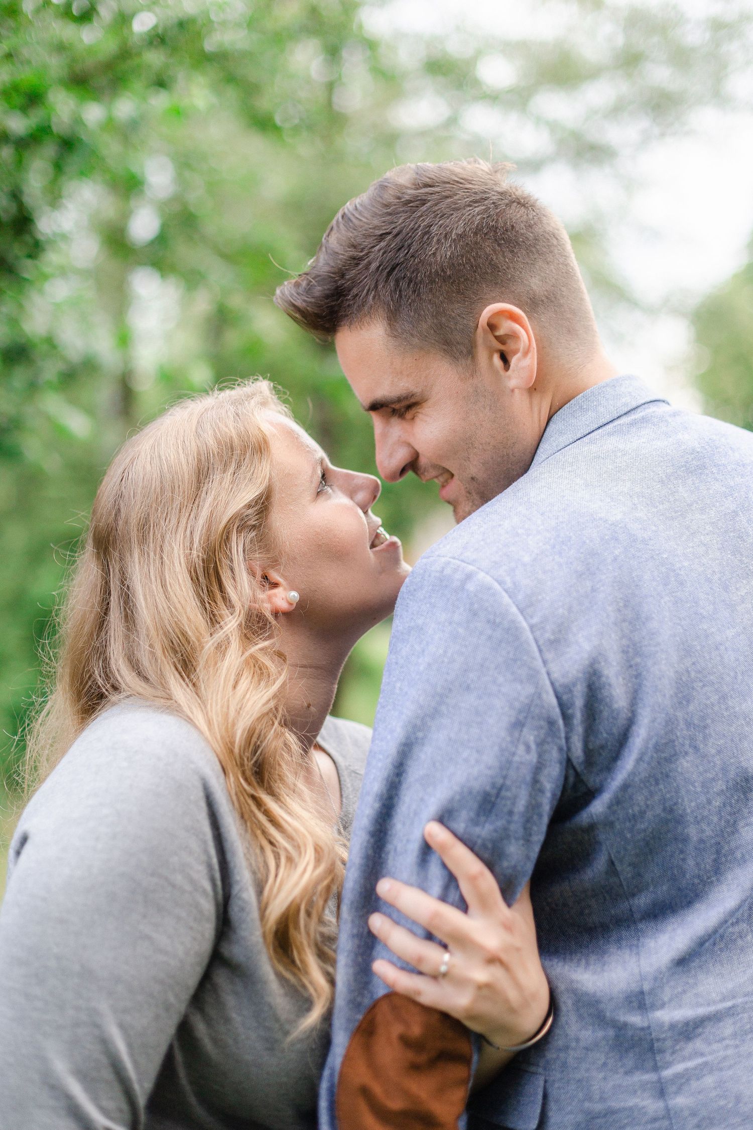 A romantic couple embraces outdoors in a tender moment against a soft green natural background - Verlobung Paar Shooting Aarau