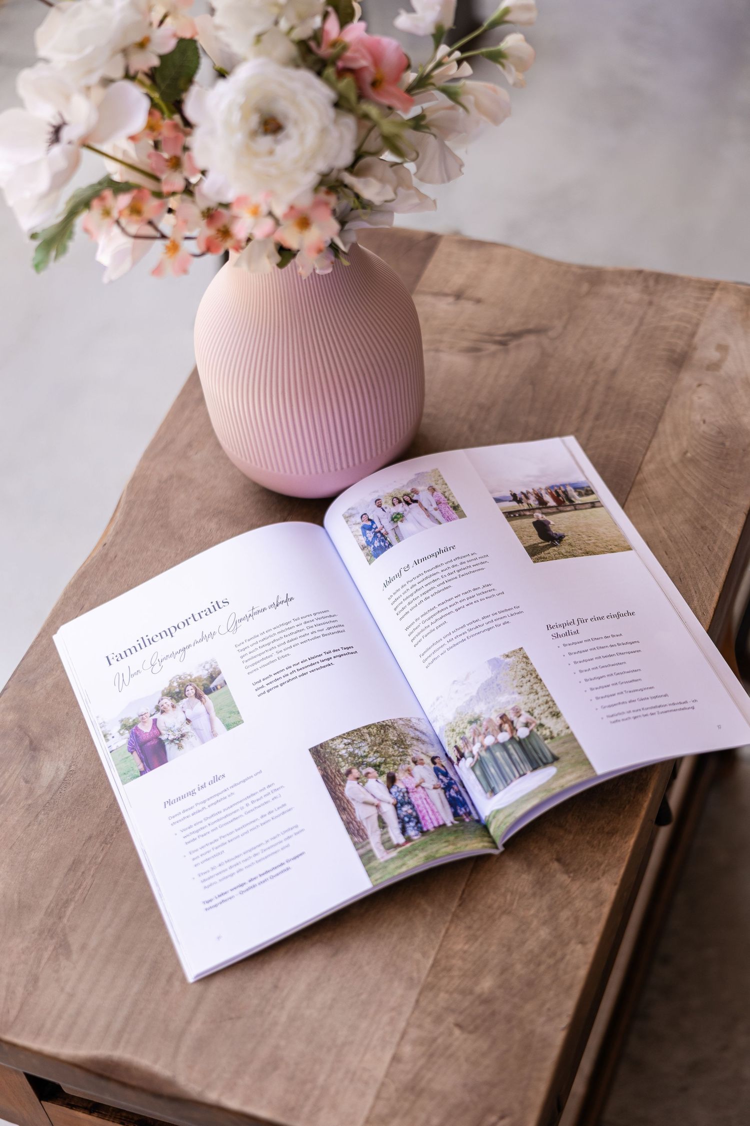 Open wedding photography magazine on wooden table beside pink ribbed vase with white and pink flowers.