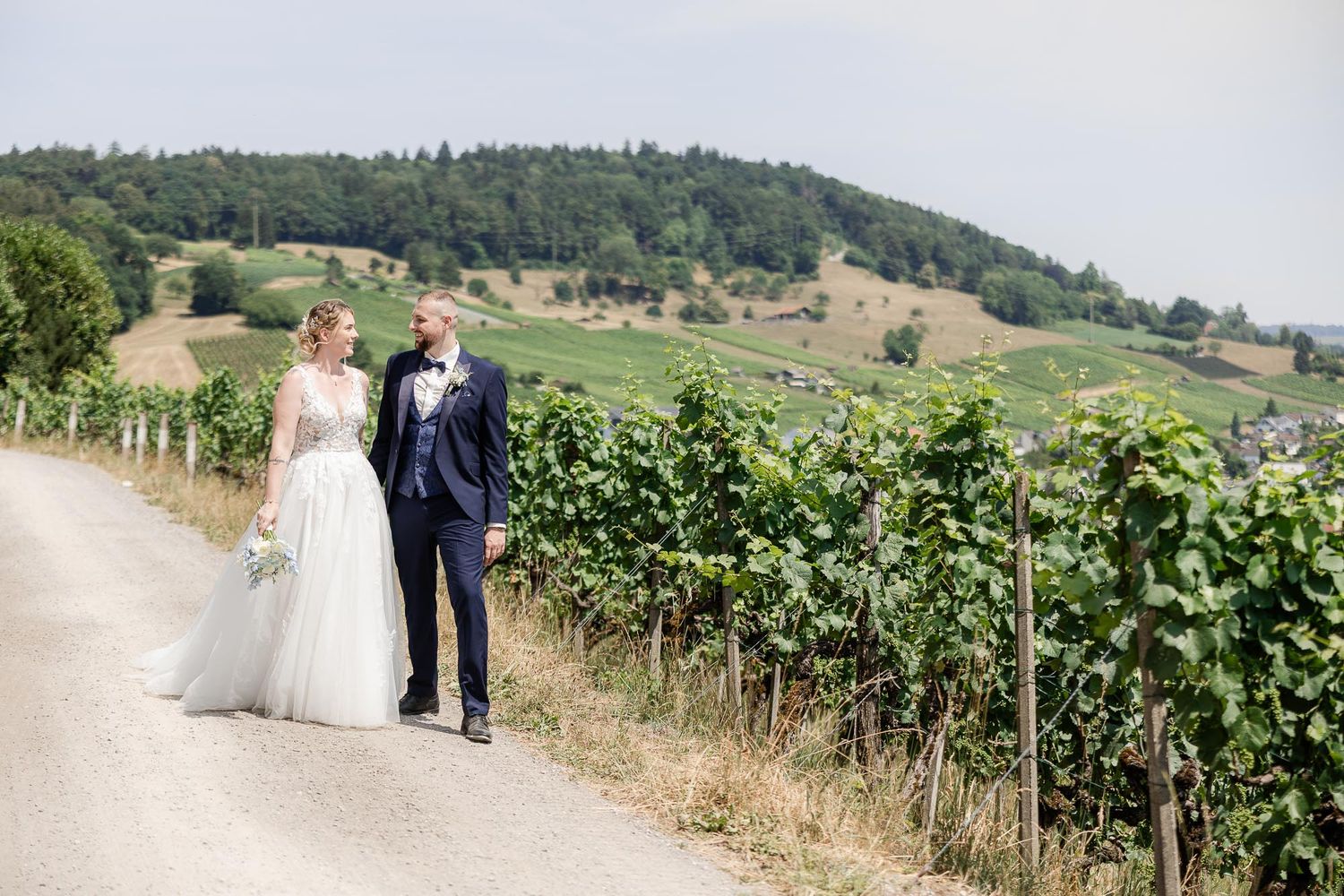 Bride and groom walking along a vineyard path with rolling green hills in the background on their wedding day.