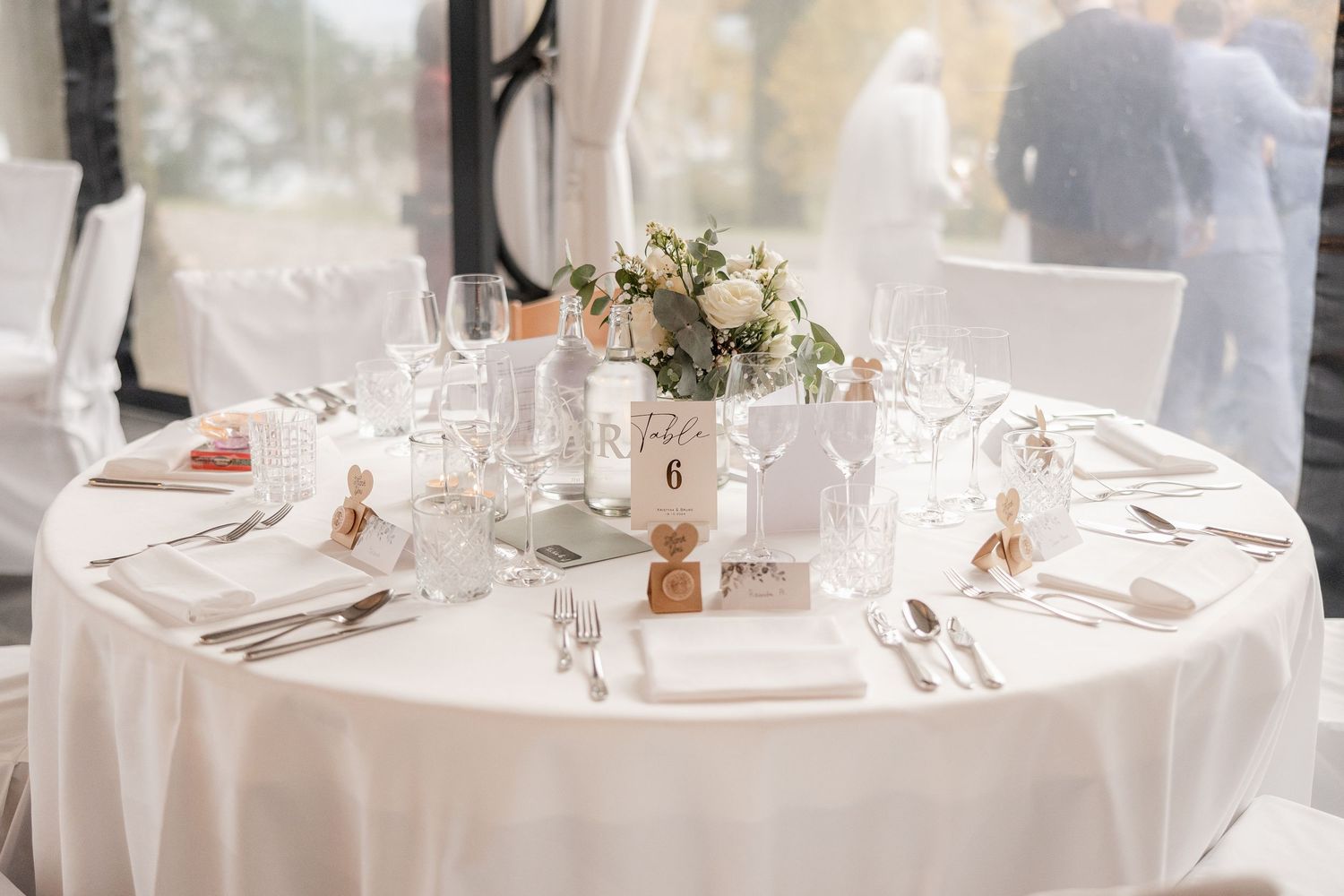 An elegant wedding table setting with white linens, crystal glassware and a delicate floral centerpiece in muted tones.