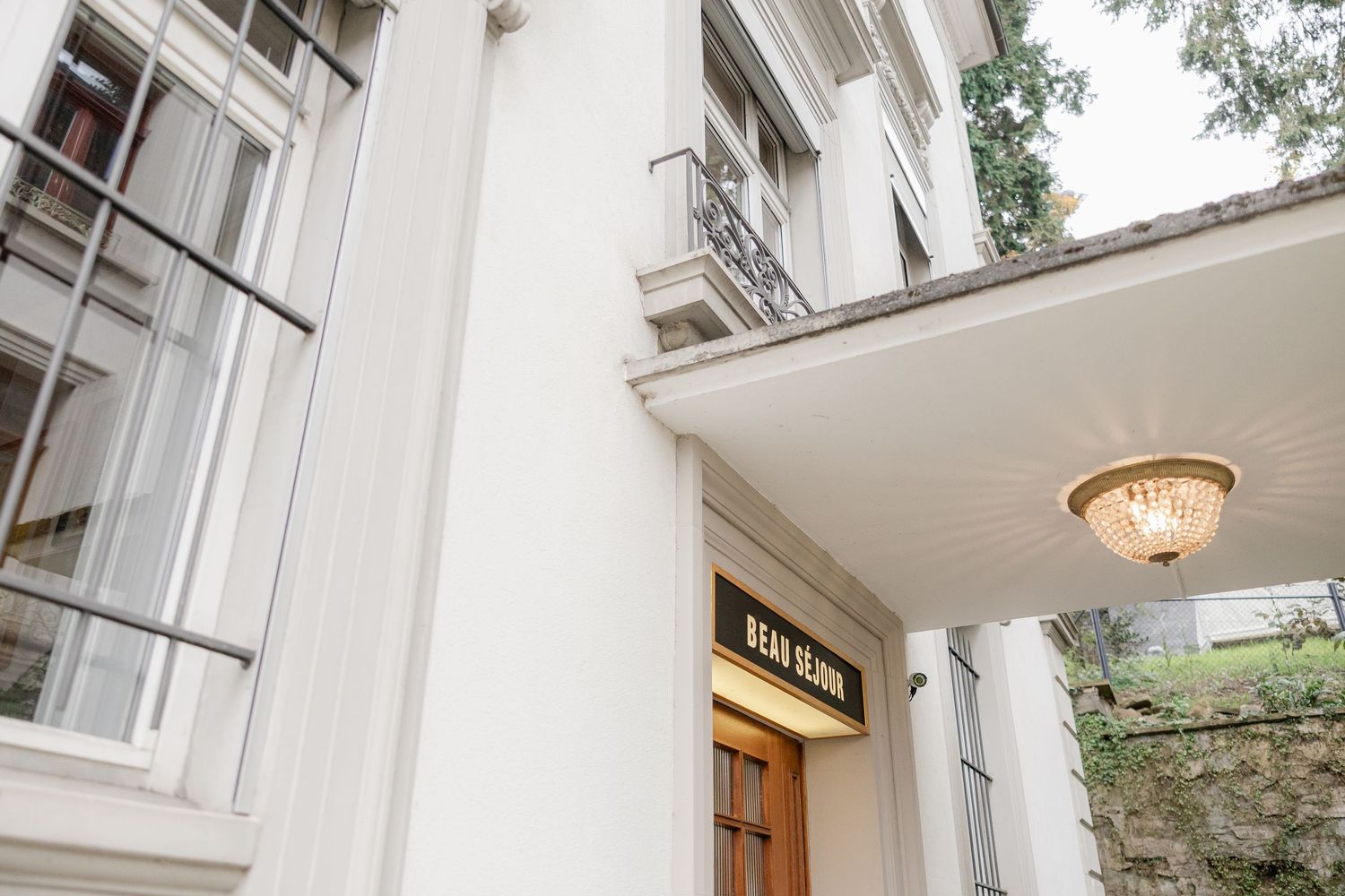 A bright white hallway with classical columns and architectural details features a pendant light fixture and wooden doors.