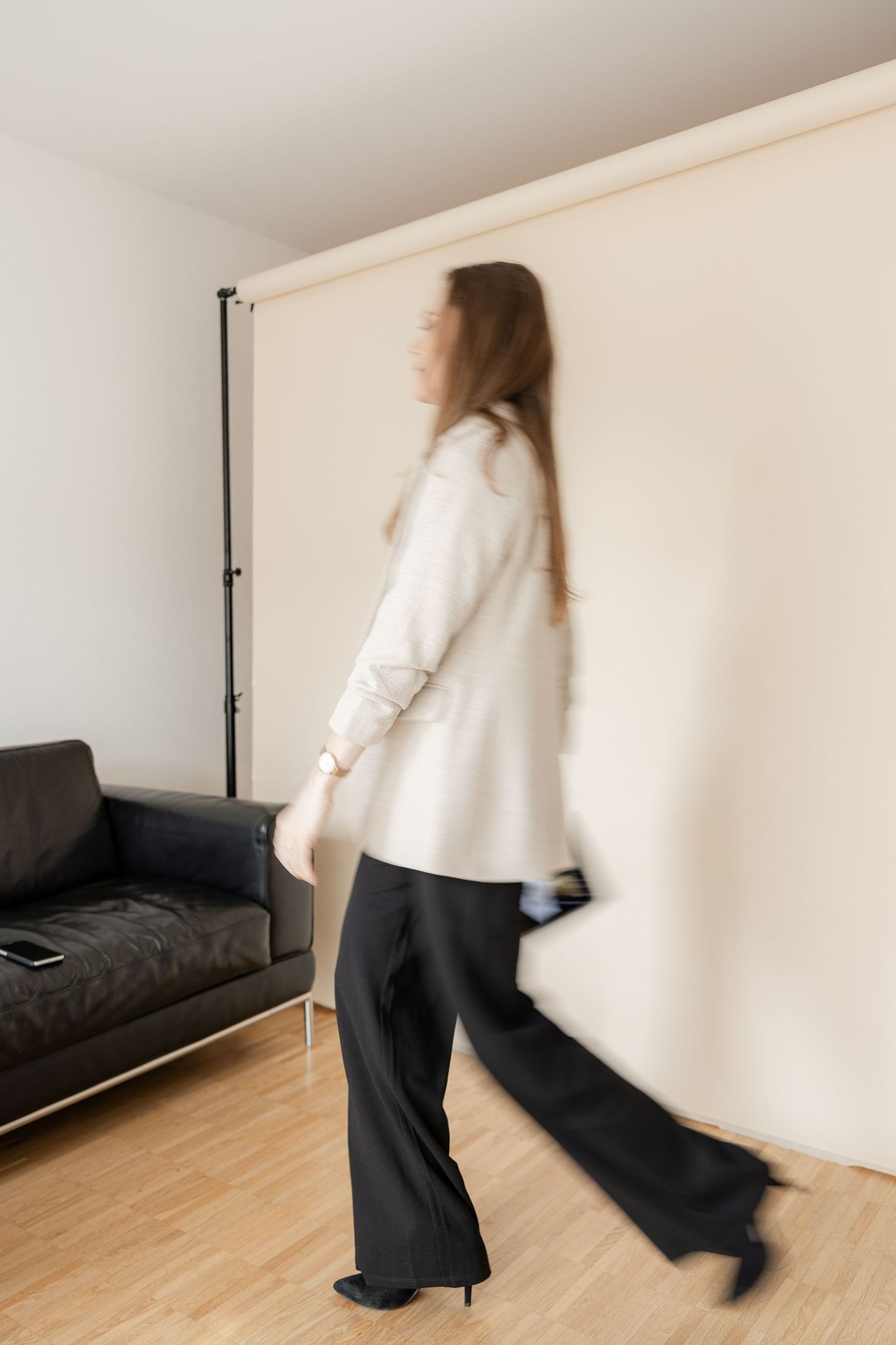 A sequence of motion blur photos showing someone in a white sweater and dark pants moving across a minimalist room interior.