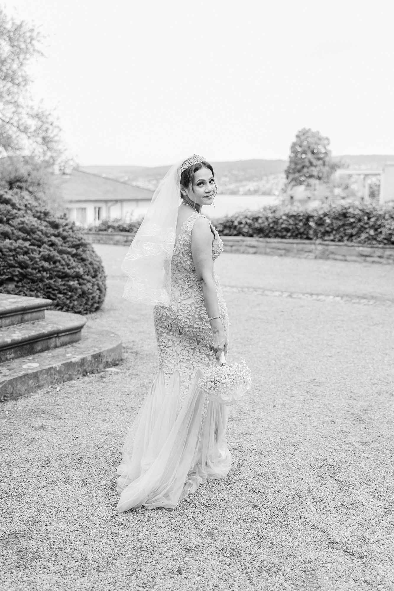 Black and white wedding photo of a bride in a sparkly gown posing outdoors in a garden setting.