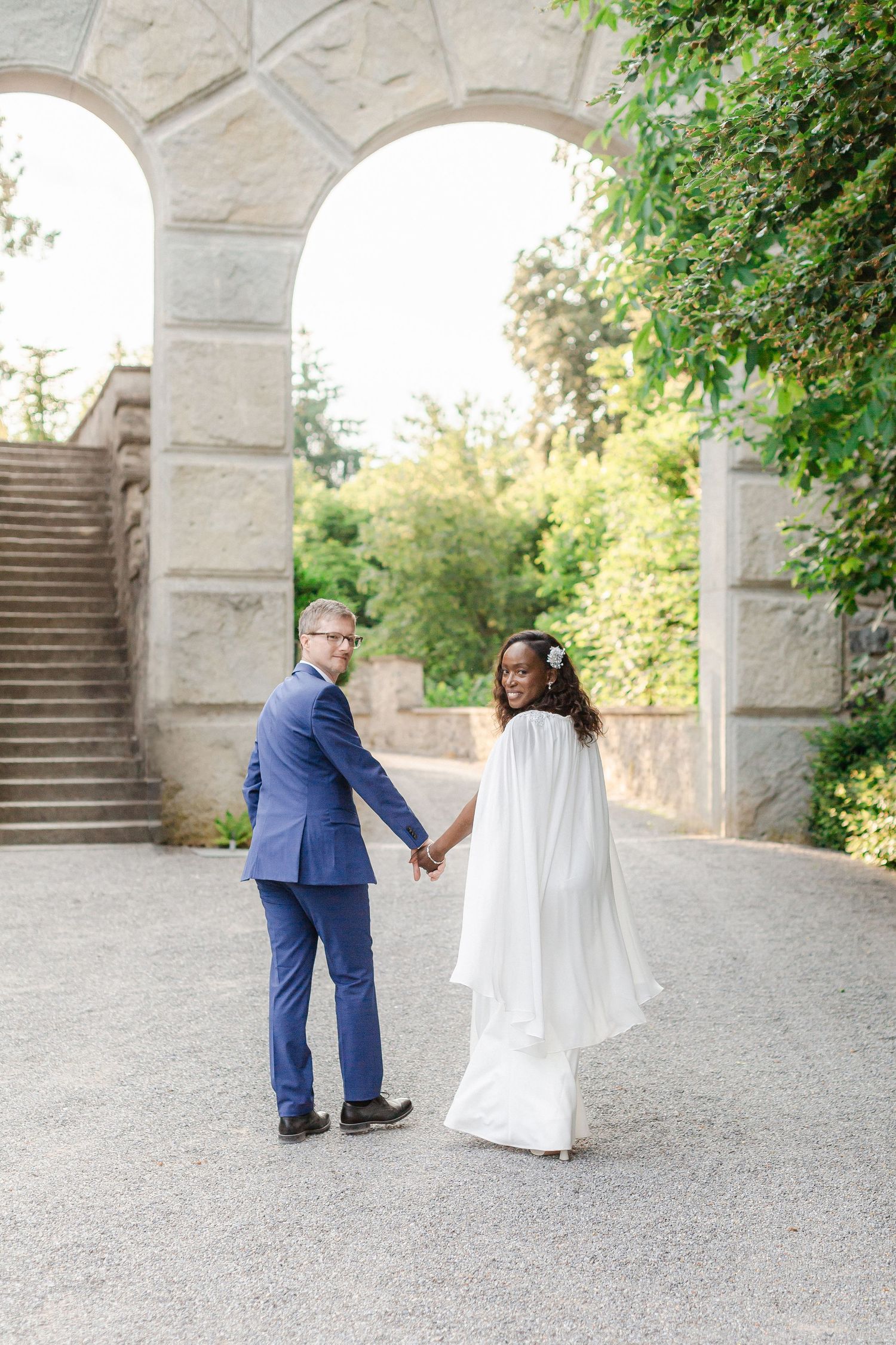 A sequence of romantic wedding photos showing a couple in formal attire under stone arches during a playful kneeling scene.