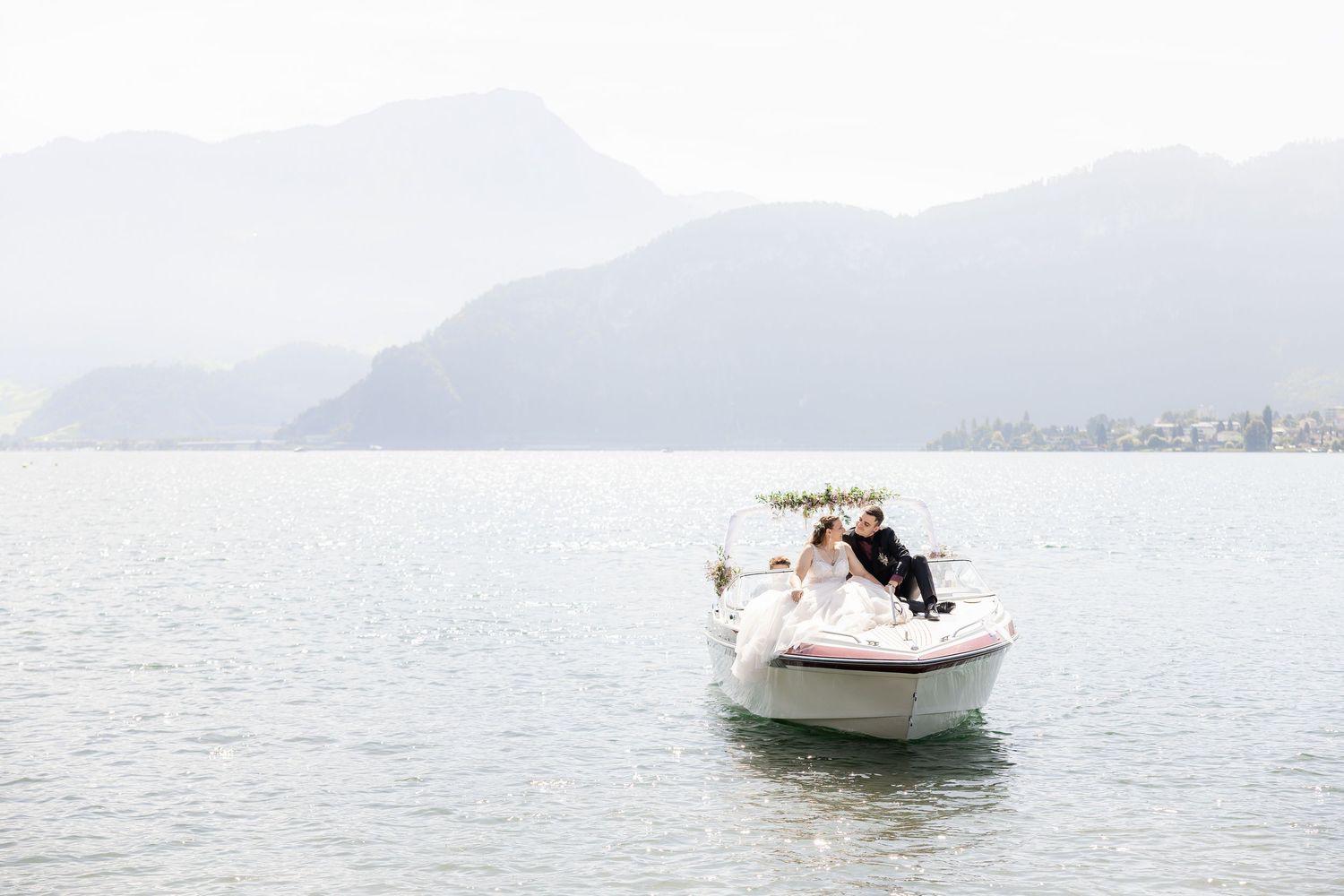 A white boat cruises across calm waters near misty mountains on a serene morning.