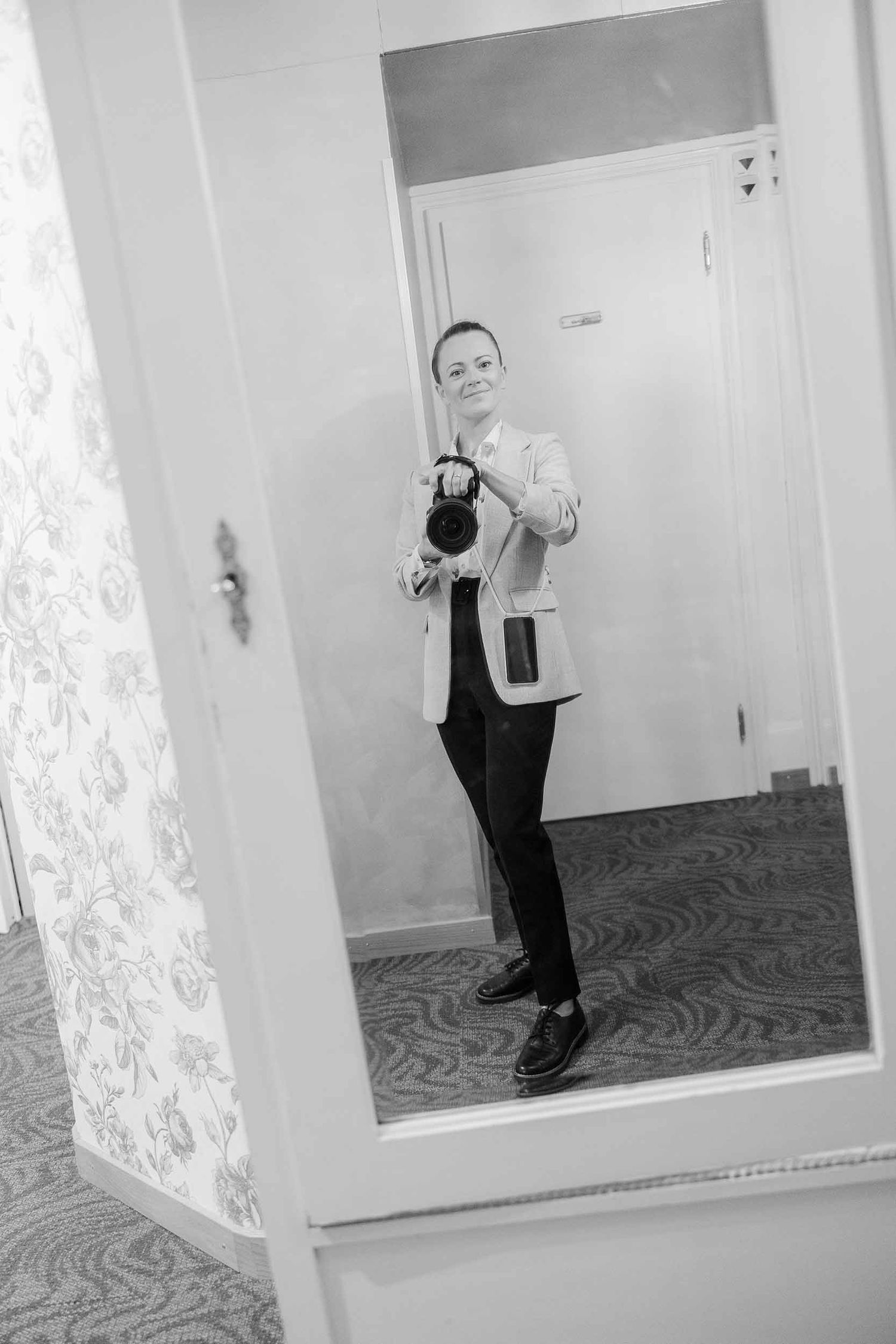 A person takes selfies in a mirror while posing in different positions against a white wall with carpet flooring.