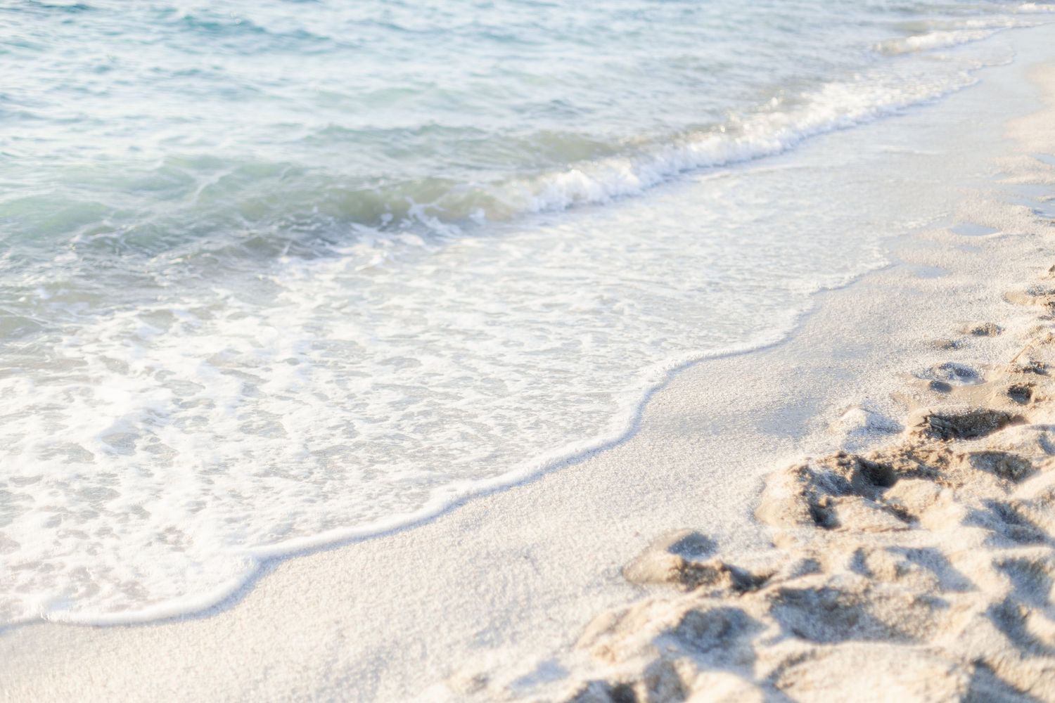 Gentle waves wash up on a pristine white sandy beach with crystal clear turquoise water stretching to the horizon.