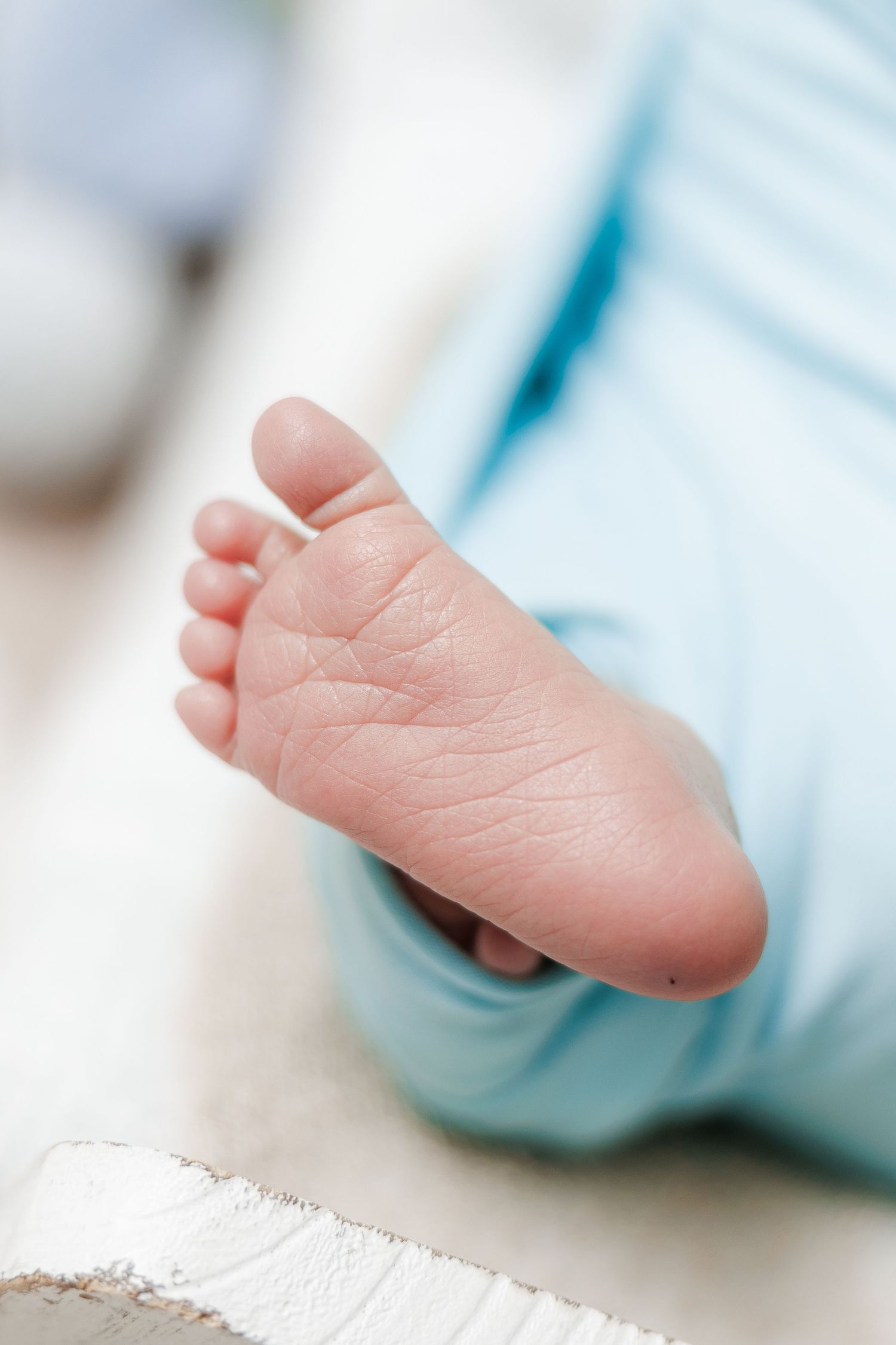 Close-up of tiny newborn baby feet wrapped in soft blue blanket showing delicate toes and skin texture.
