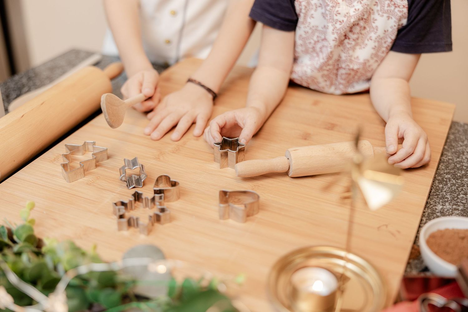 Hands rolling out gingerbread cookie dough with a wooden rolling pin on a floured wooden surface.