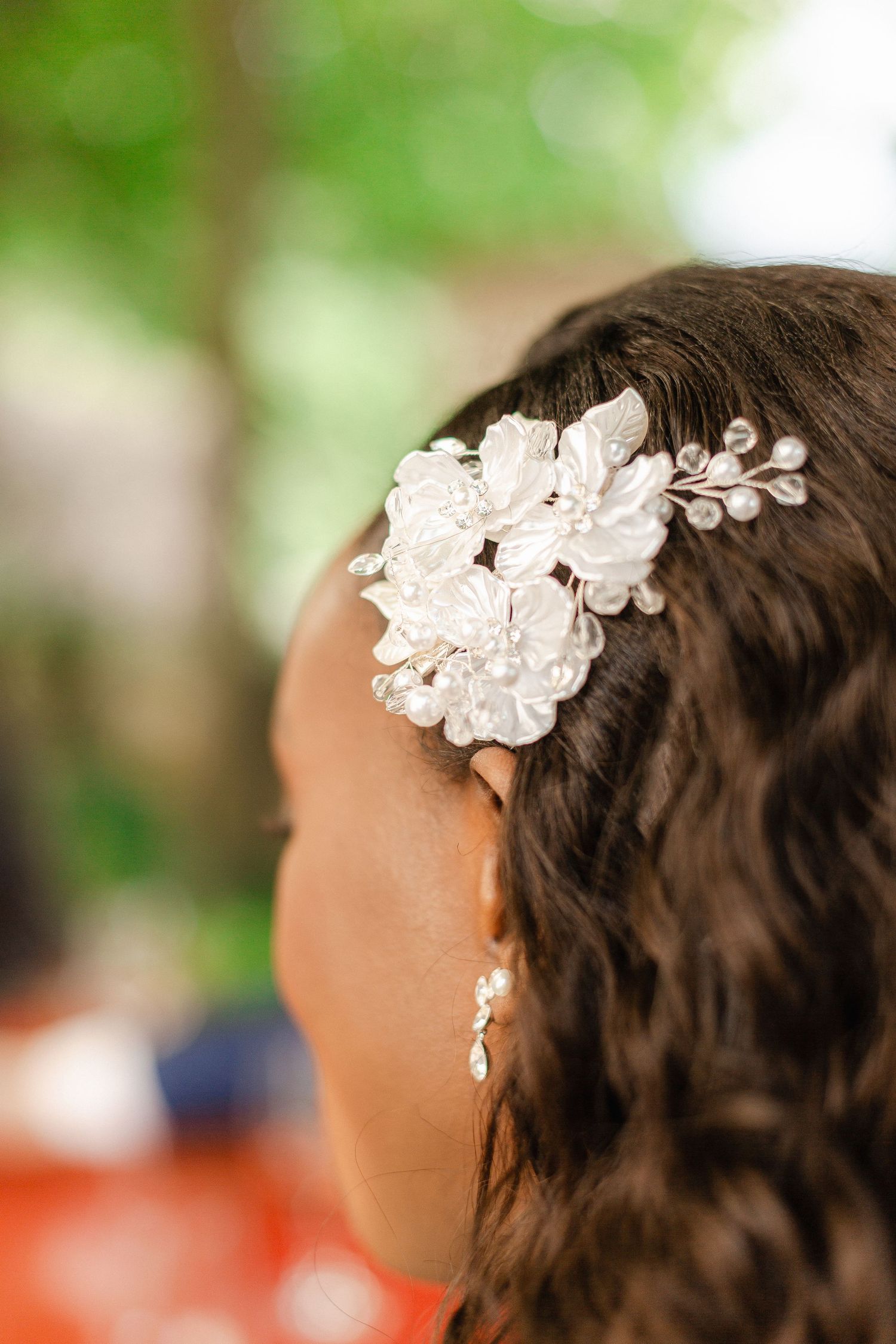 Beautiful white lace floral hair accessory adorns dark curly hair against a soft green outdoor background.