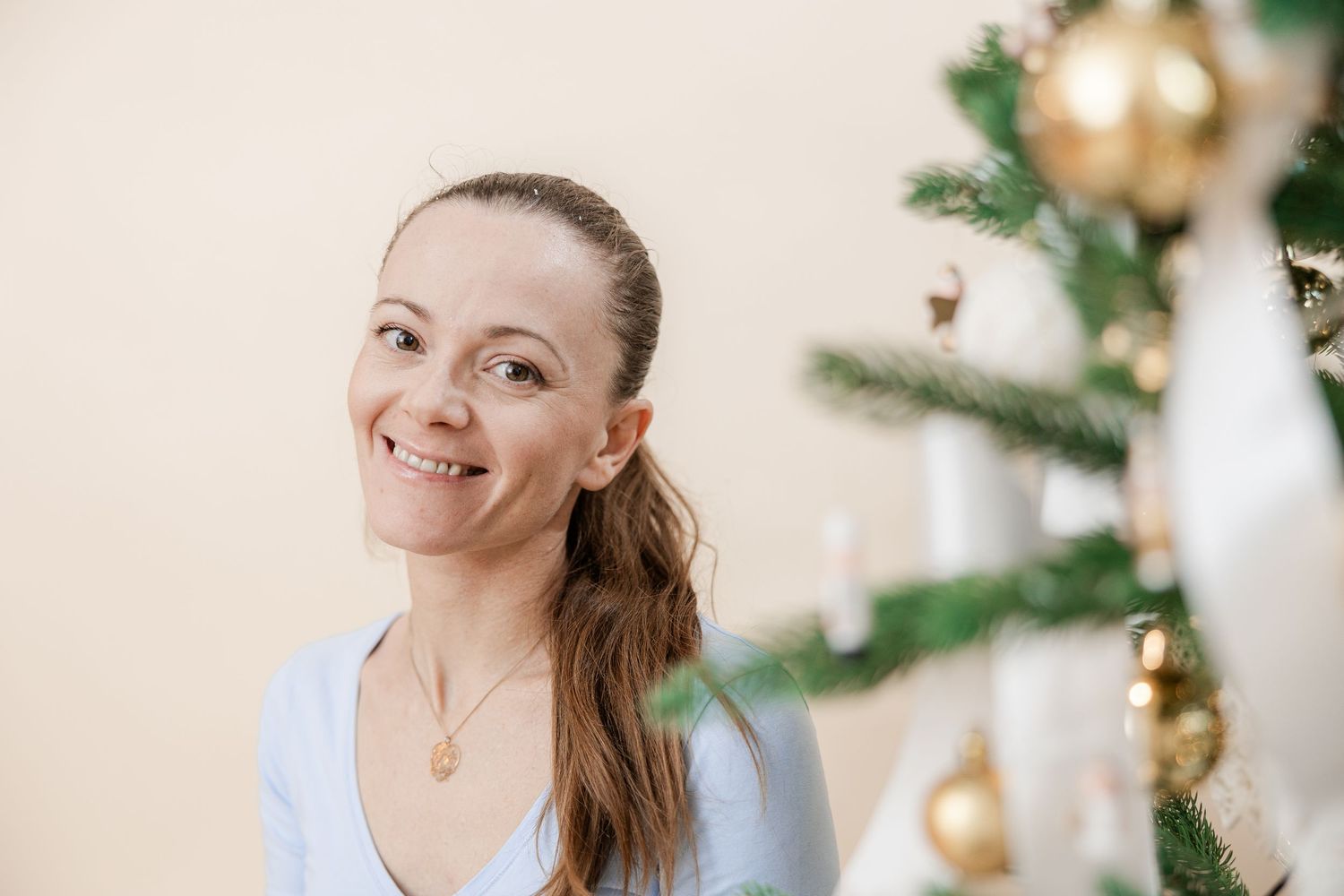 Woman in white sweater smiling near Christmas decorations and golden ornaments in festive holiday setting.