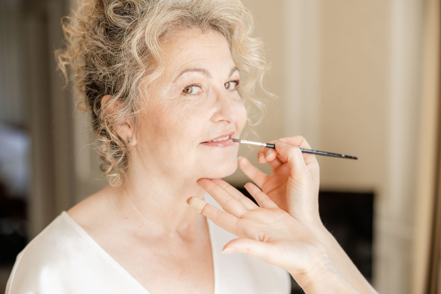 Mature woman having lipstick applied with a brush by a makeup artist during a professional beauty session.
