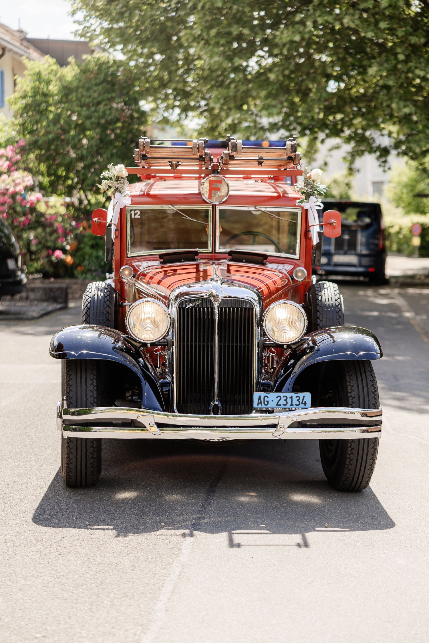 Front view of a vintage red Chrysler luxury car with chrome grille and headlights parked on pavement.