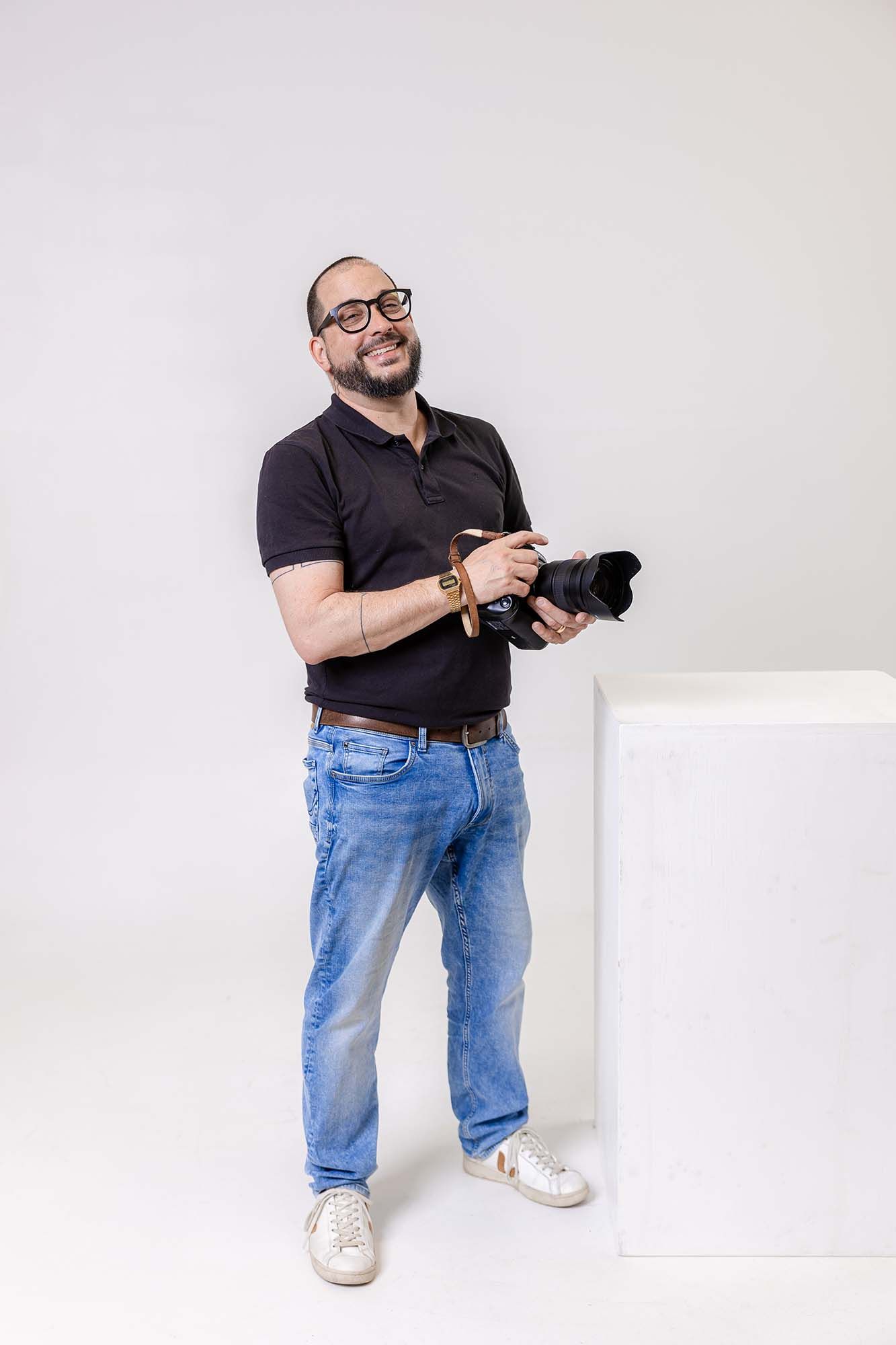Professional photographer in black polo and jeans poses with camera against white background in three creative angles.