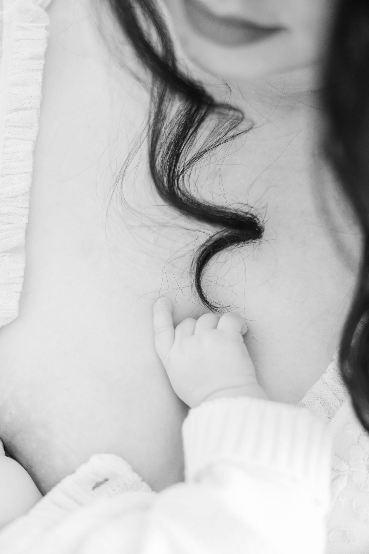 A tender black and white close-up of a tiny baby hand reaching up to grasp dark curly hair.