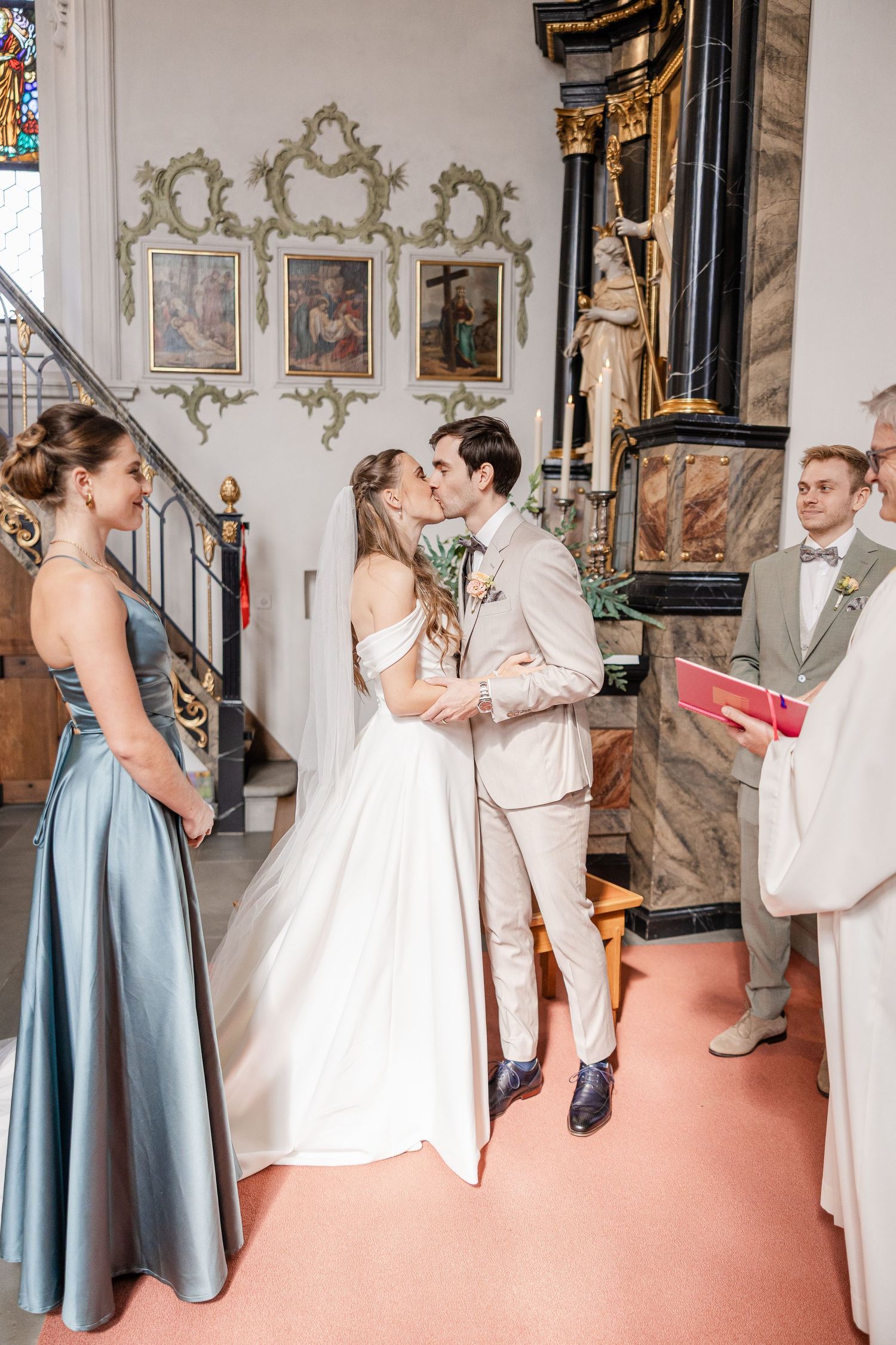 Wedding couple shares a romantic dance sequence in an ornate church with blue-dressed bridesmaid looking on.
