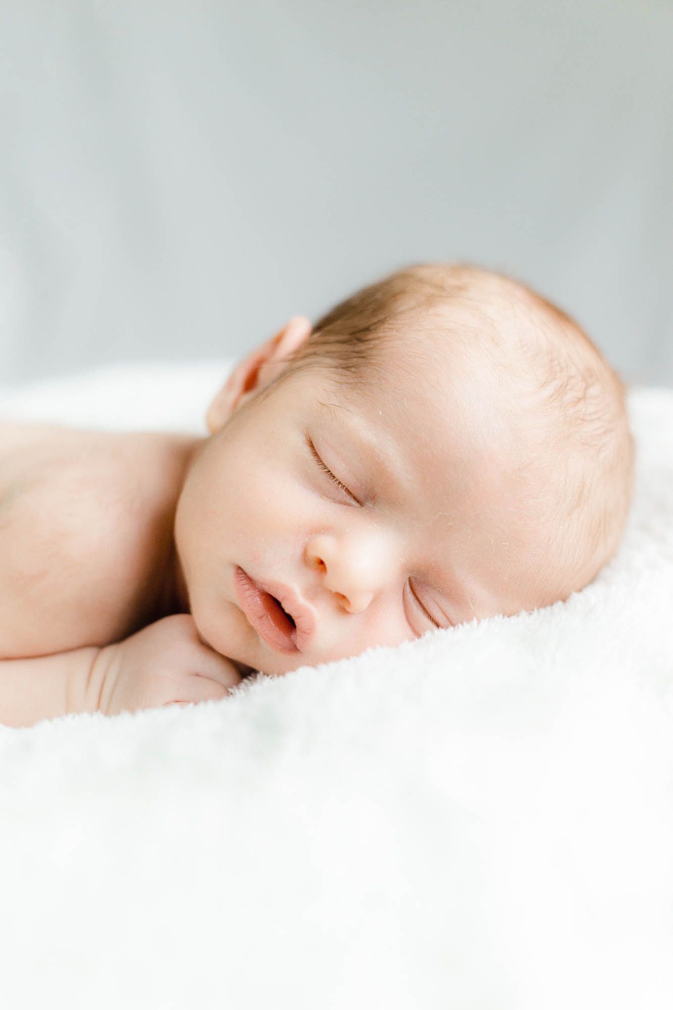 Peaceful sleeping newborn baby wrapped in soft white blankets against light neutral background. Baby Fotograf Aarau, Schweiz