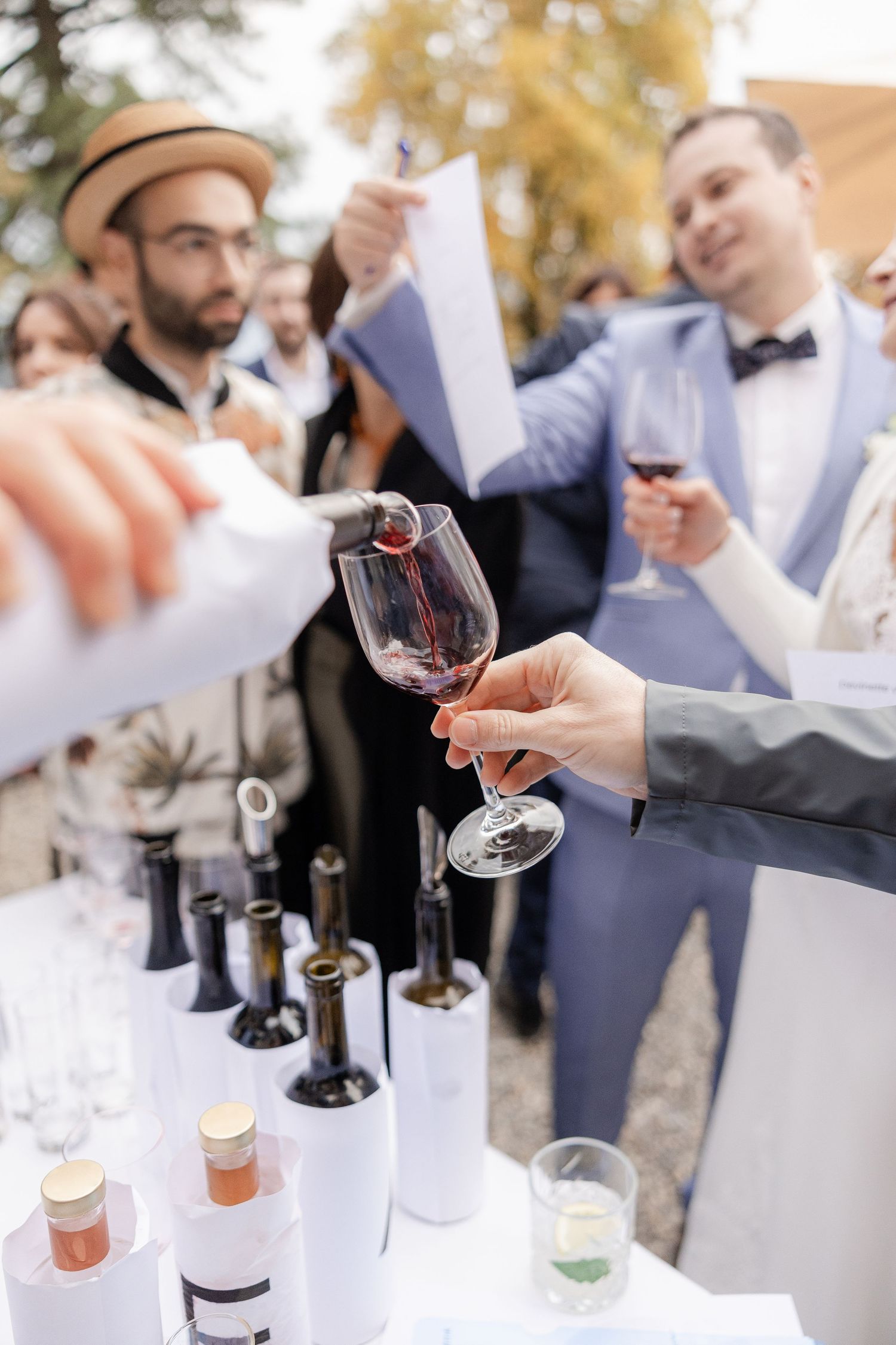 Wine tasting event with guests sampling drinks as bottles line up on white tablecloth at outdoor gathering - Hochzeitsfotograf Luzern