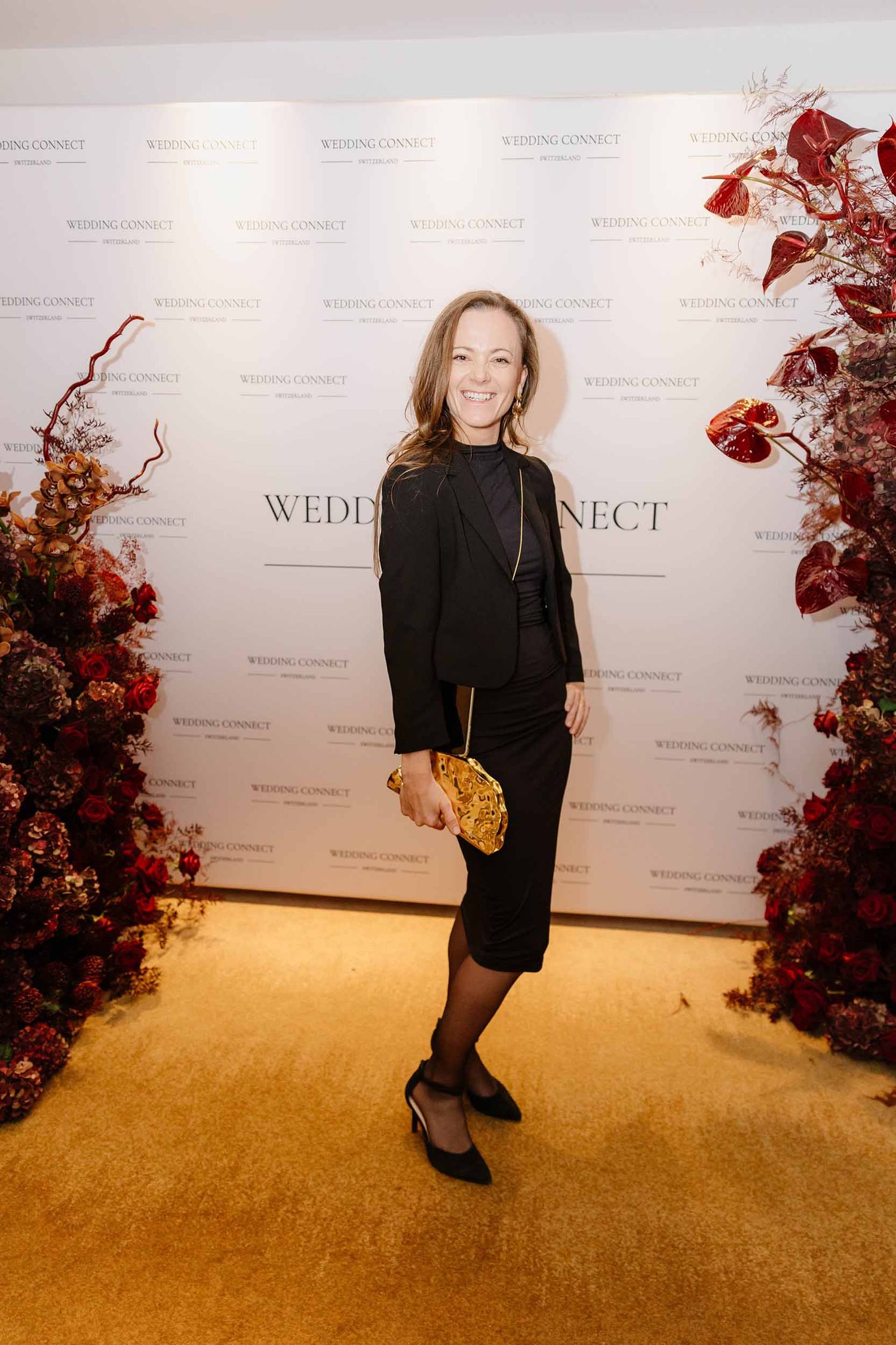 Someone in black attire poses against a white backdrop with autumn-themed floral decorations at a Wedding Connect event.