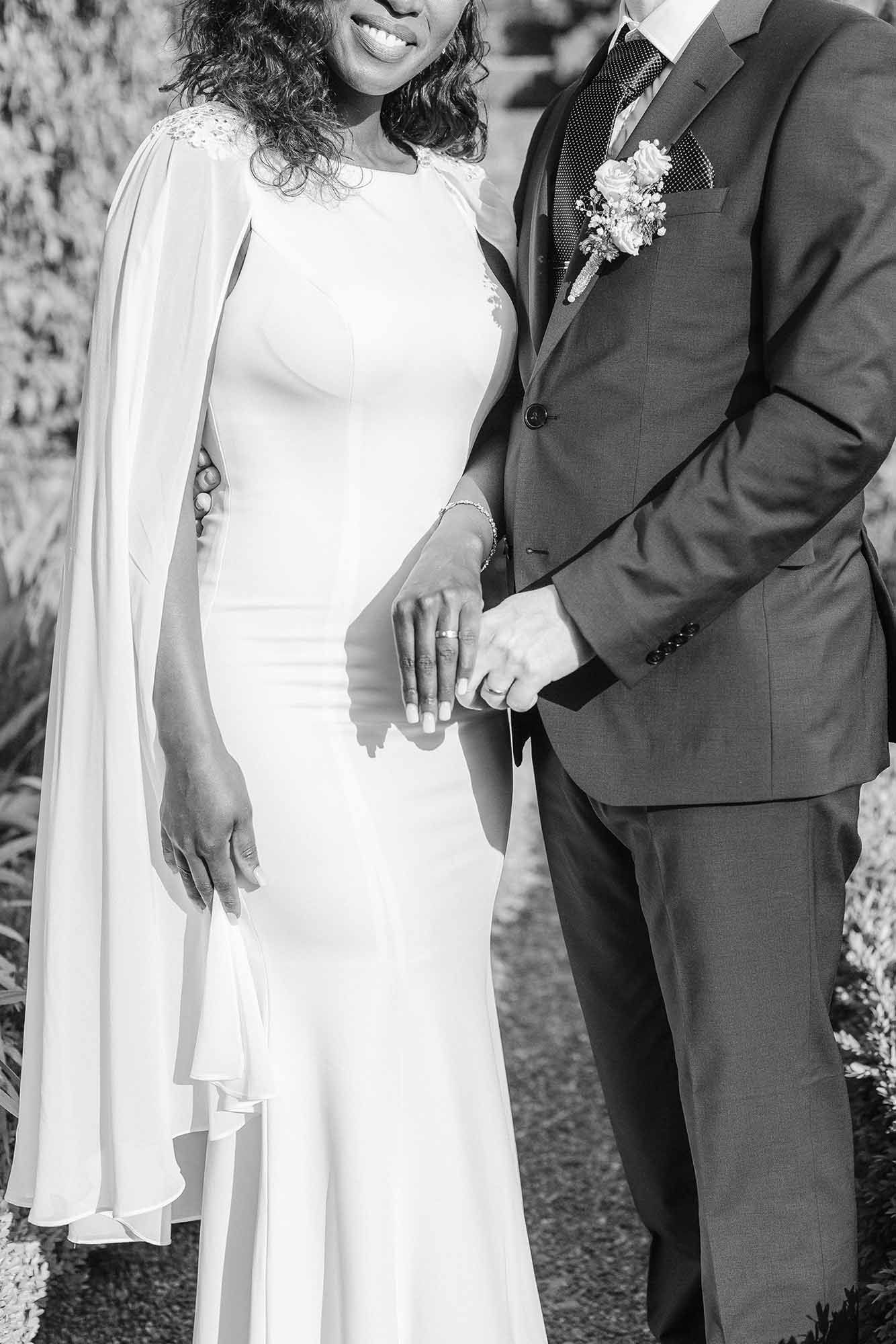 A black and white wedding photo showing a couple in formal attire standing together outdoors.