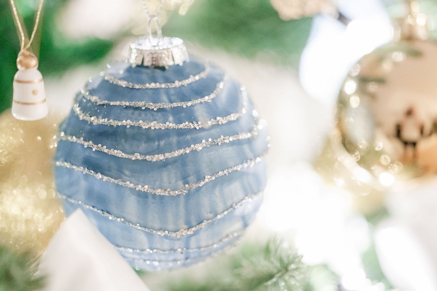 Elegant blue glass Christmas ornaments with glittery silver stripes hanging against a soft bokeh background.
