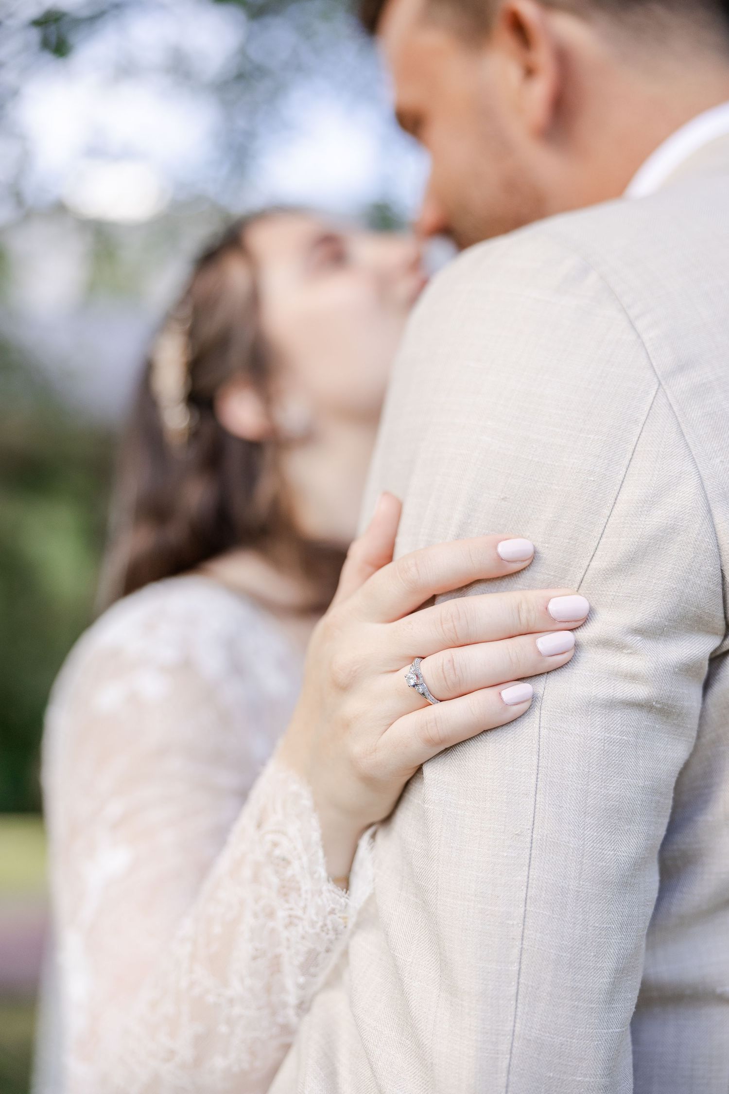 A romantic wedding couple embraces in soft natural light wearing white and light gray formal attire.