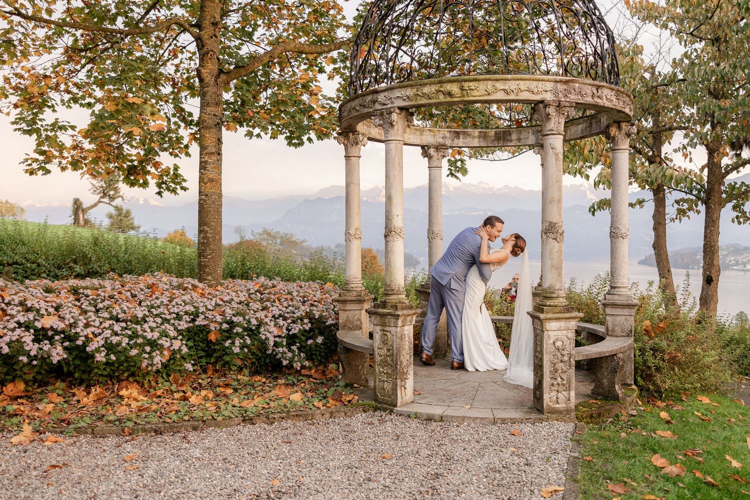 A romantic couple embraces during their autumn wedding photoshoot with golden leaves and trees in the background.