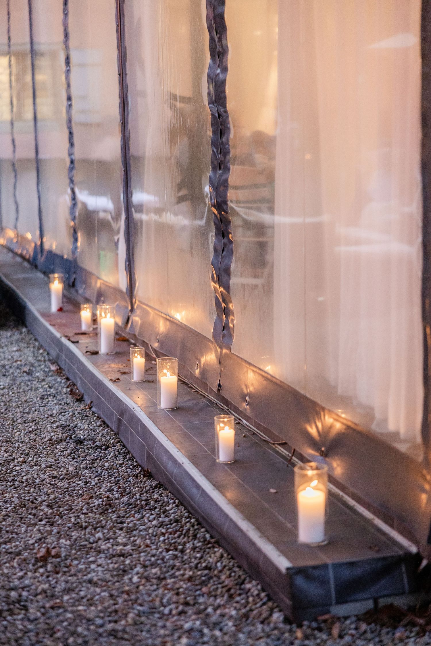 Row of glowing candles in glass holders create an elegant ambiance along a gravel-lined pathway.
