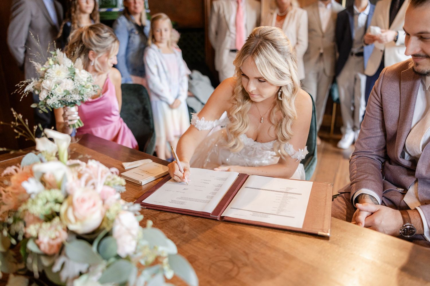 Wedding guests sign the guestbook at an elegant reception while floral centerpieces decorate the wooden tables.