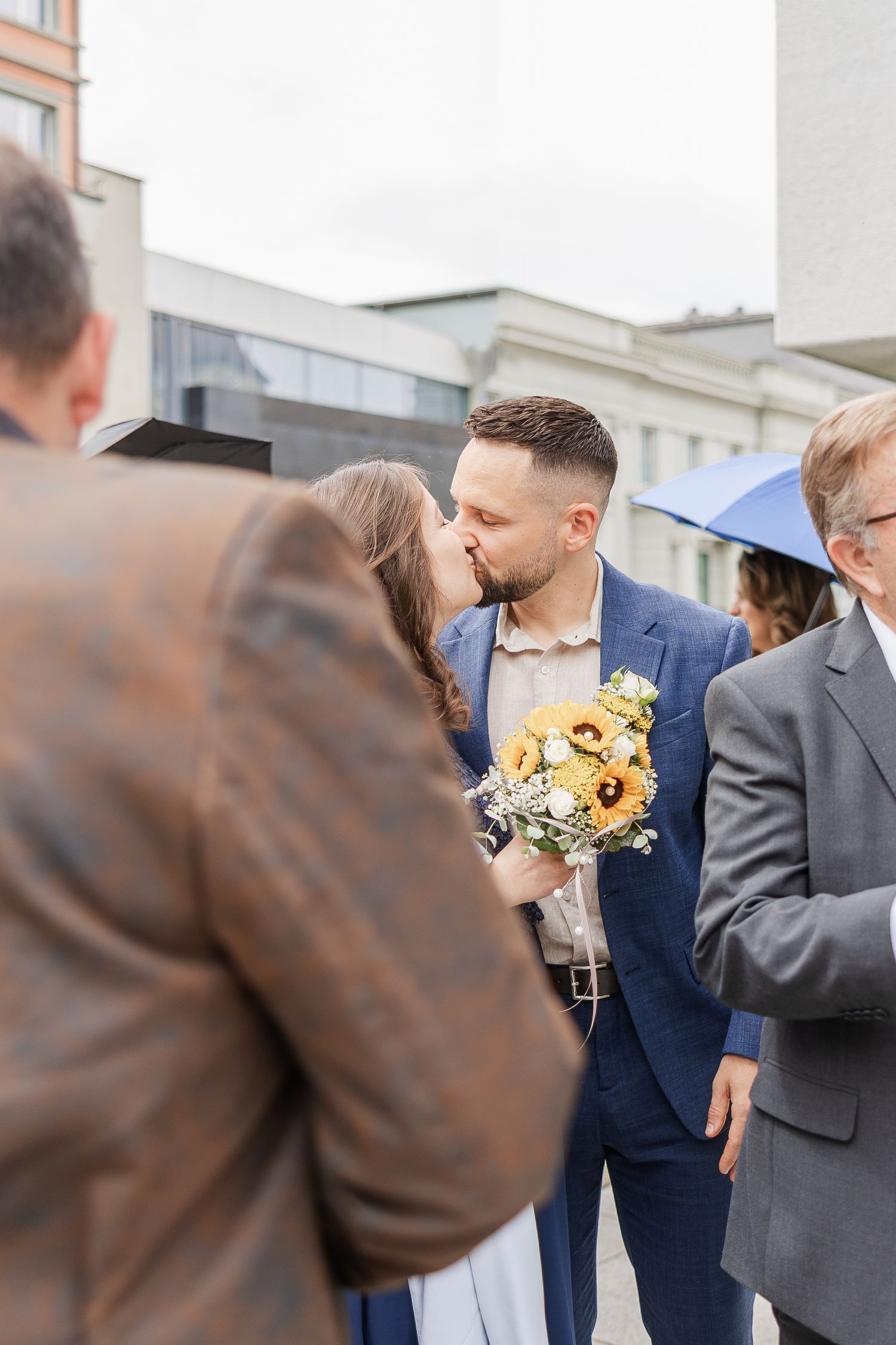 A bride and groom share a kiss at their wedding ceremony while holding bright yellow sunflower bouquet. Hochzeit Fotograf Aarau, Schweiz