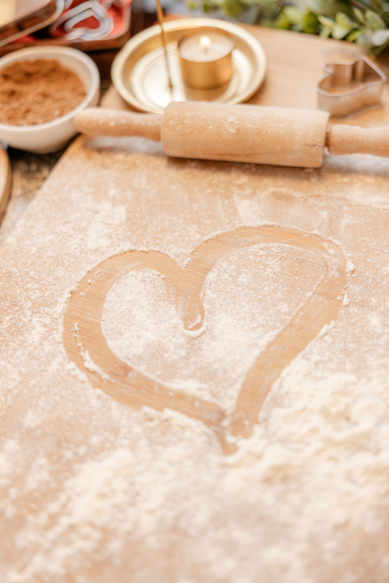 A heart shape drawn in white flour on a wooden surface with a rolling pin and baking ingredients in the background.