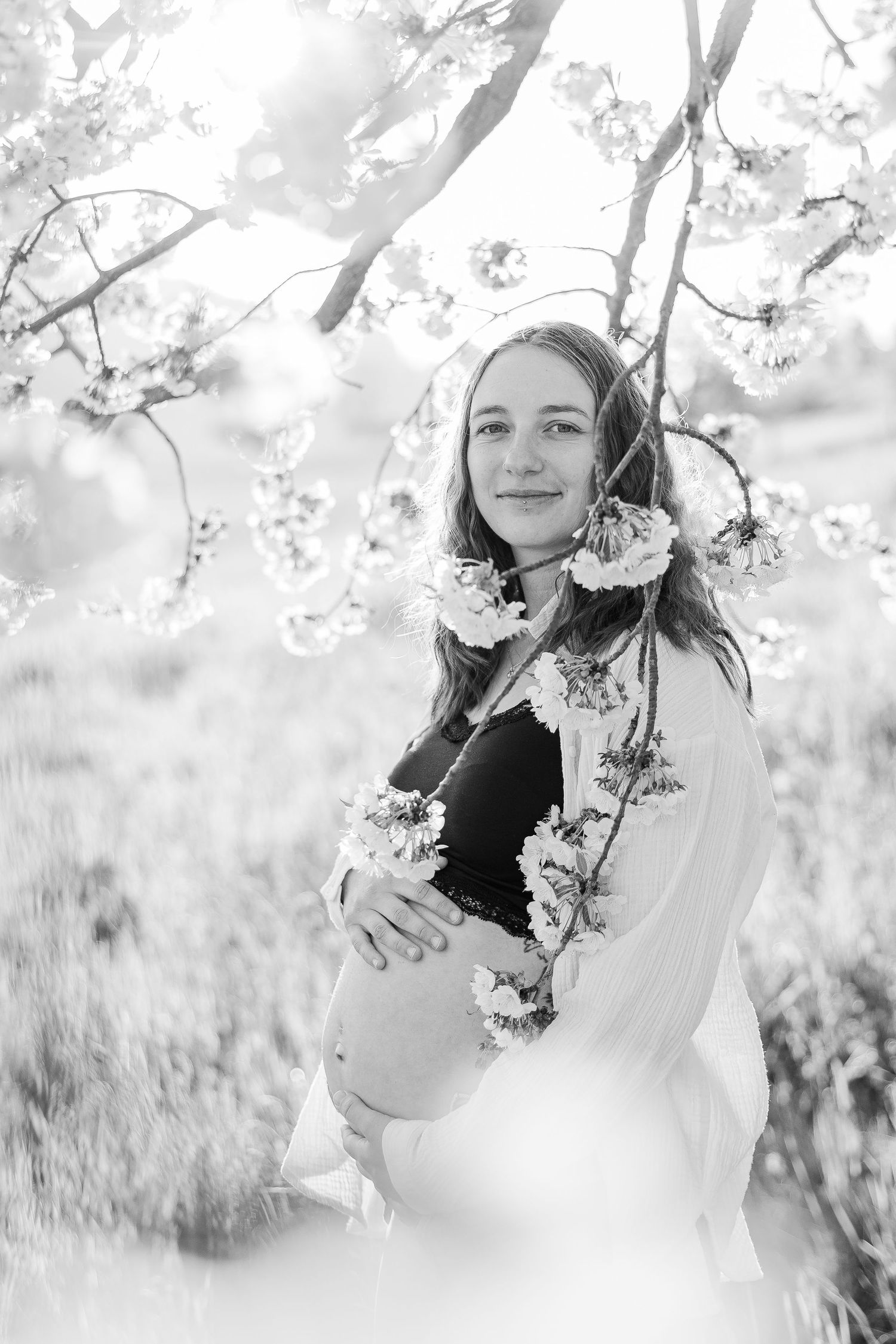 Black and white photo series showing a dreamy outdoor maternity portrait session with spring blossoms and soft natural lighting.