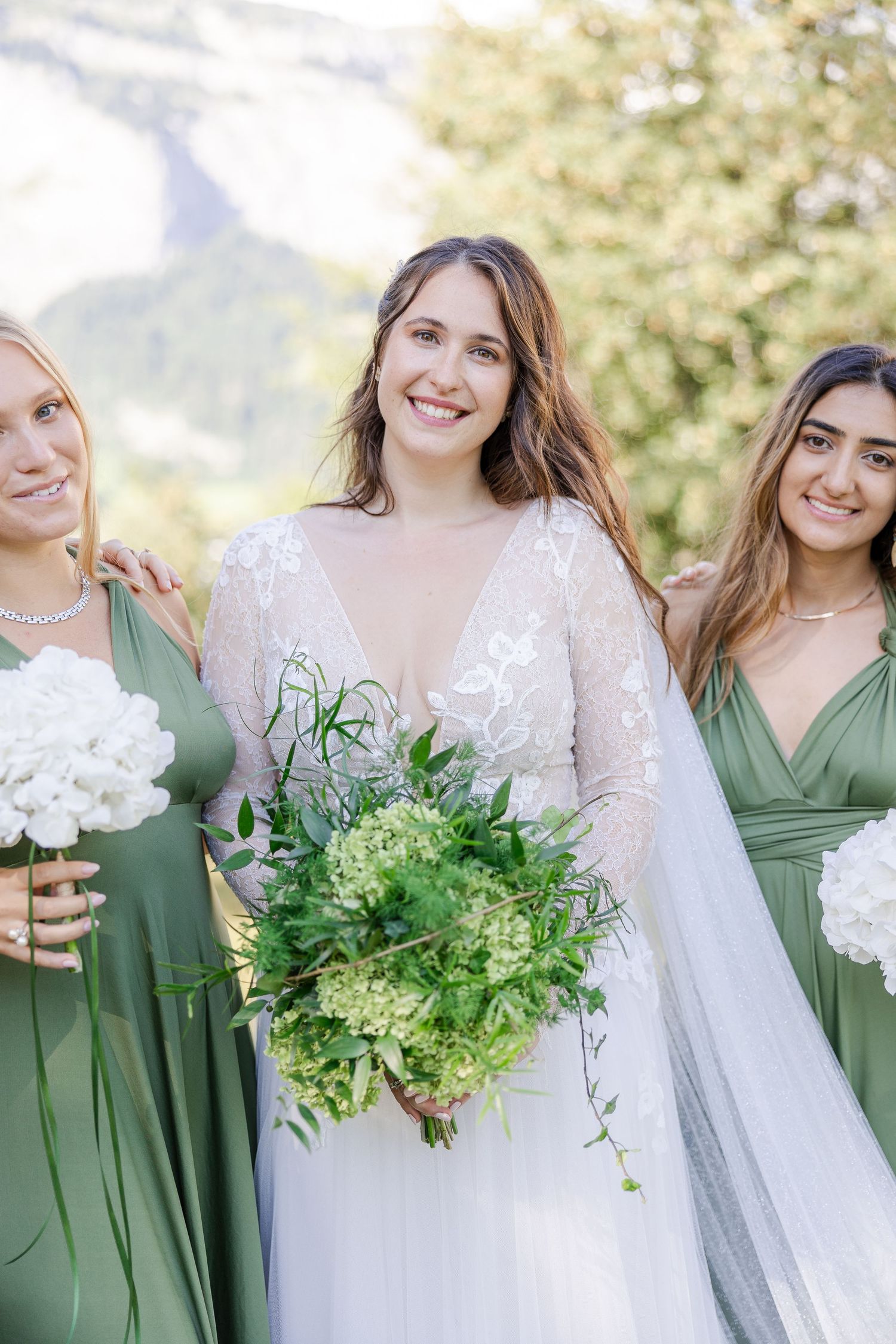 A bridal party wearing white and sage green dresses hold fresh florals with white and green bouquets. Flims, Switzerland