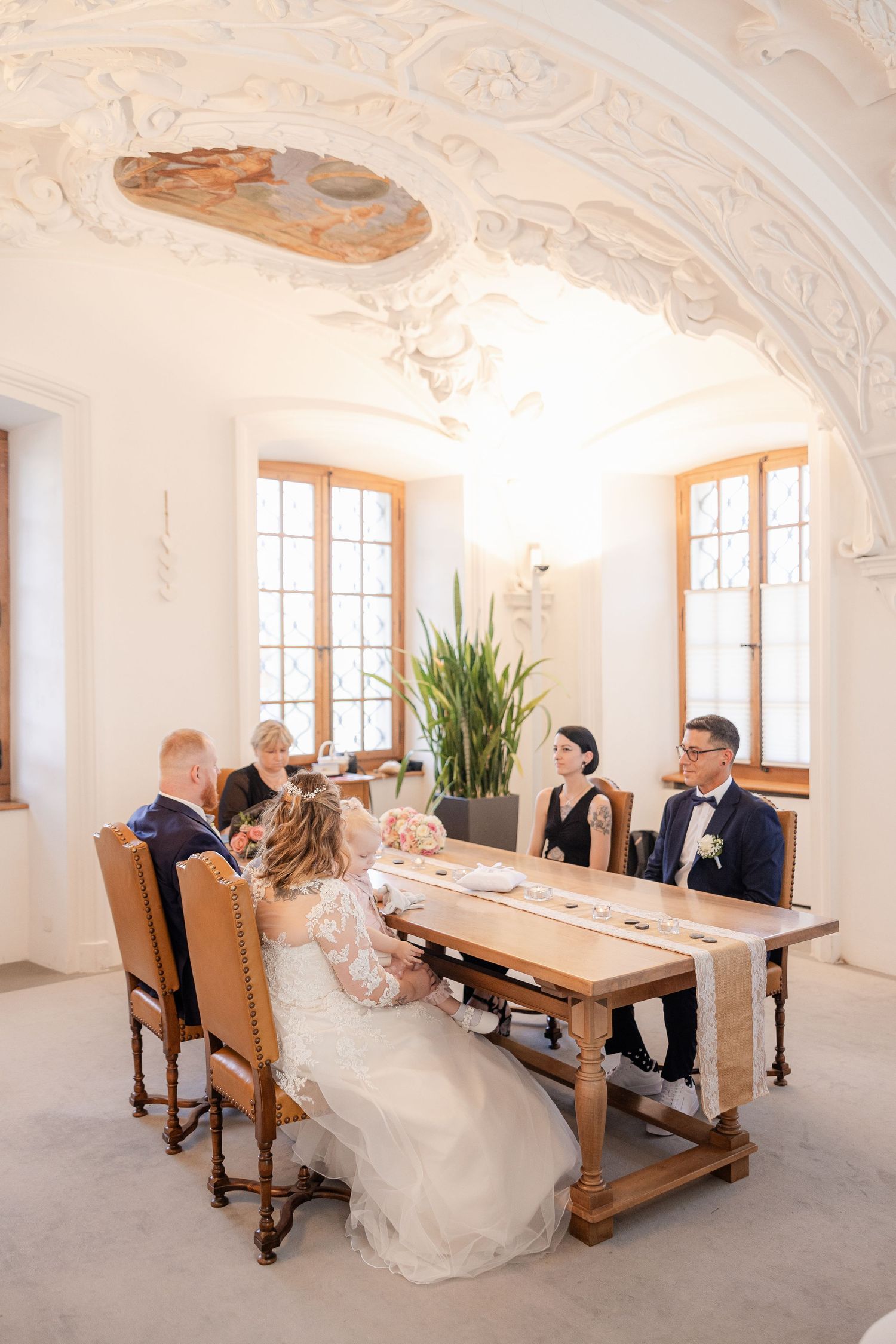 Elegant baroque-style dining room with ornate white walls and ceiling features a long wooden table with high-backed chairs.