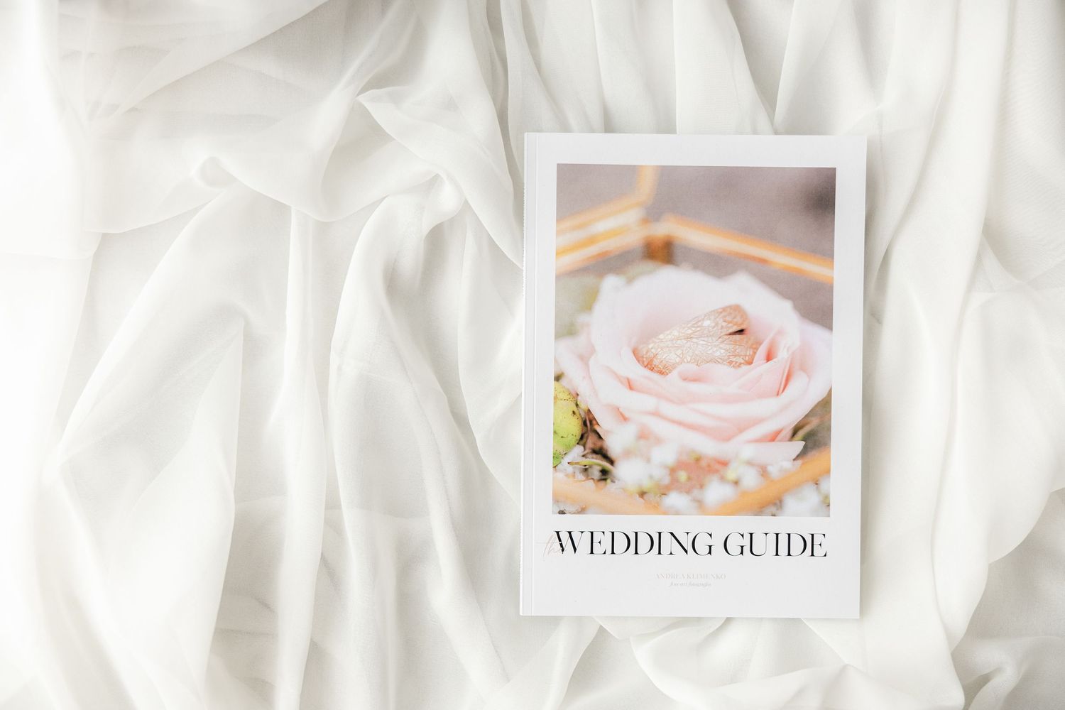 A wedding guide booklet with a pink rose and gold ring on white fabric.