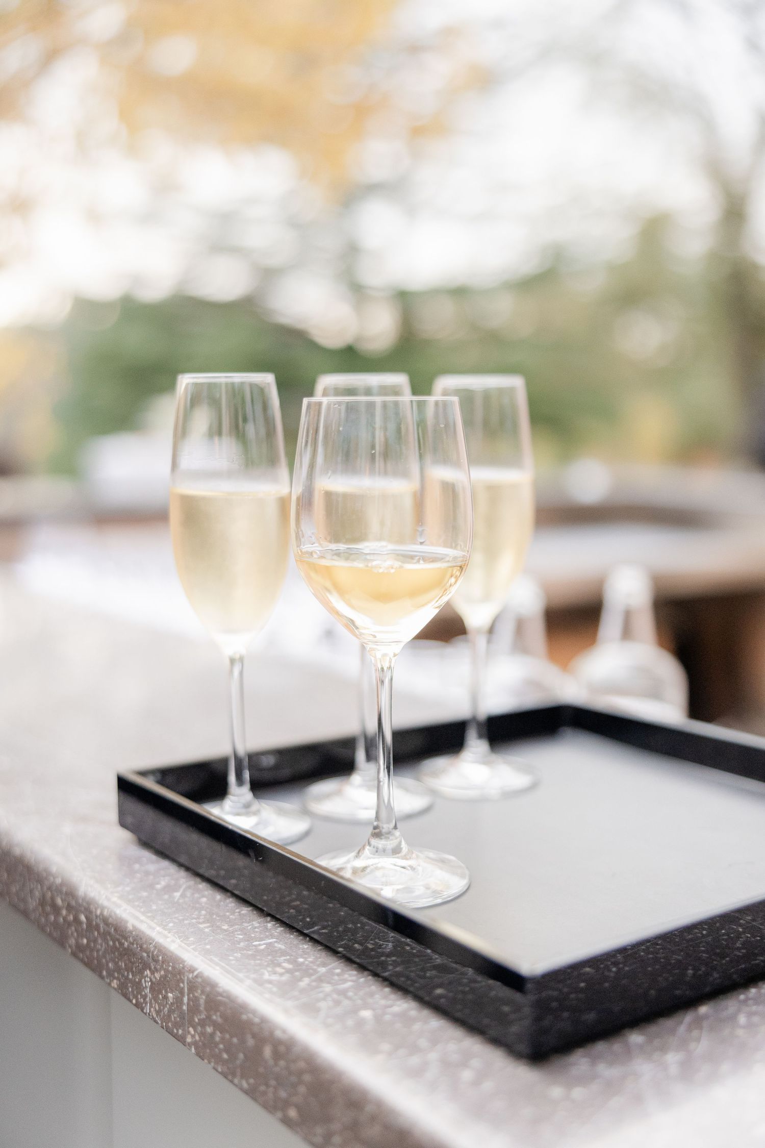 Empty wine glasses sit on a black framed serving tray against a light colored surface in an elegant setting.