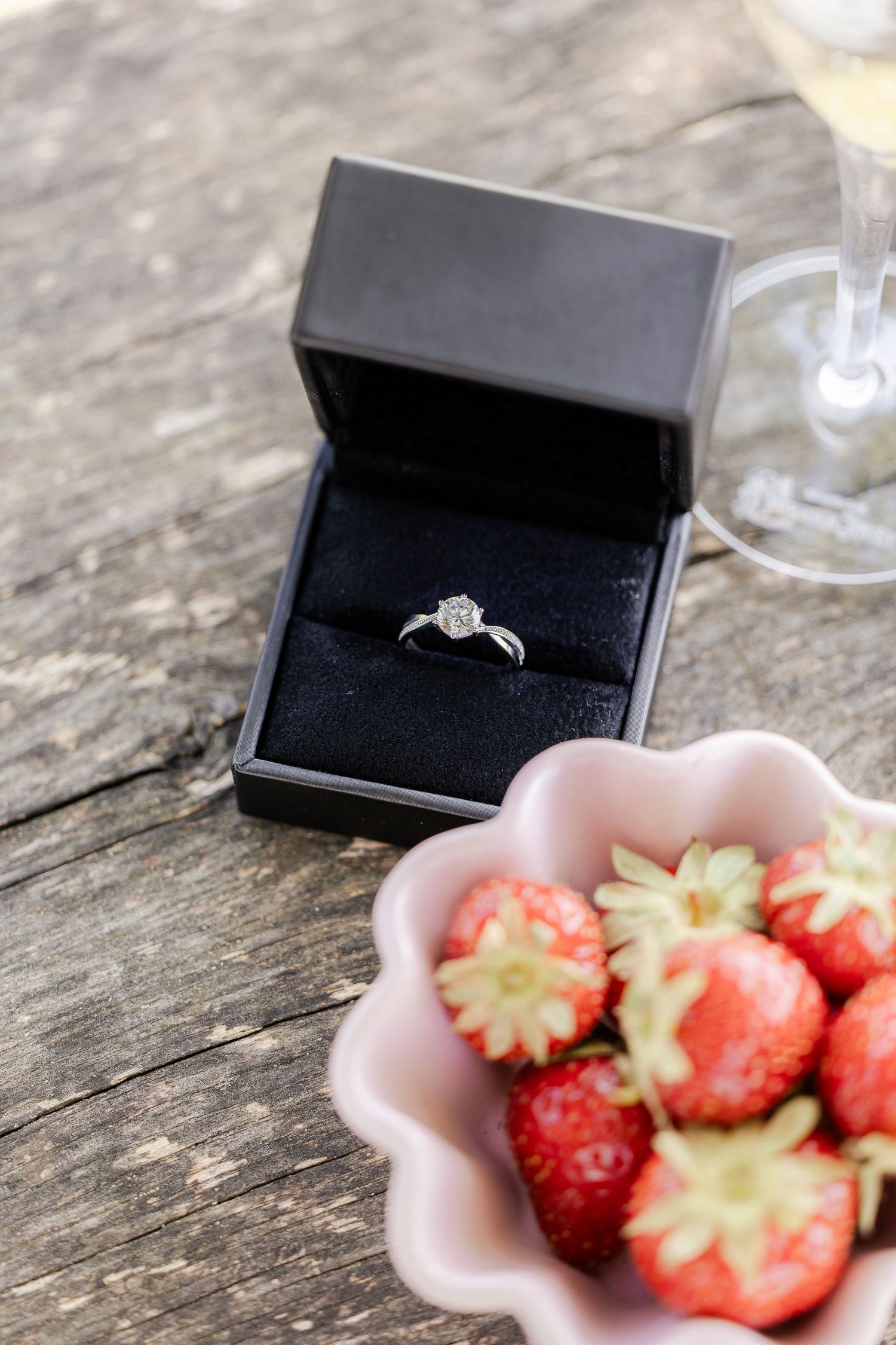 A black ring box and bowl of fresh strawberries arranged on a rustic wooden surface.