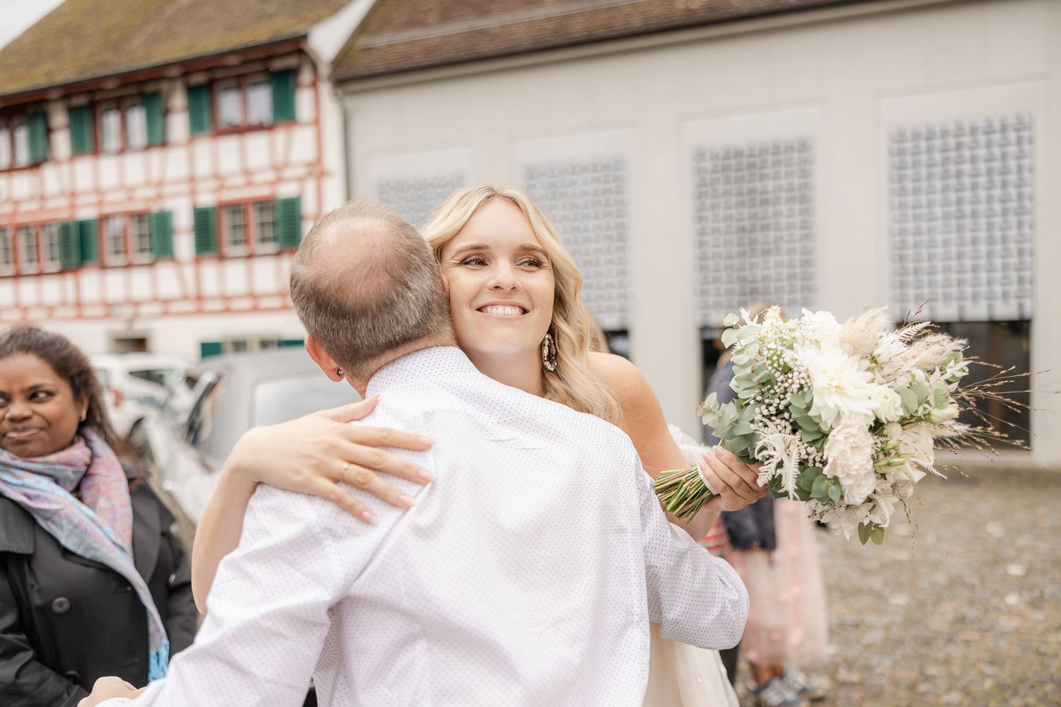Wedding guests celebrate and embrace each other during an outdoor reception by a stone wall.