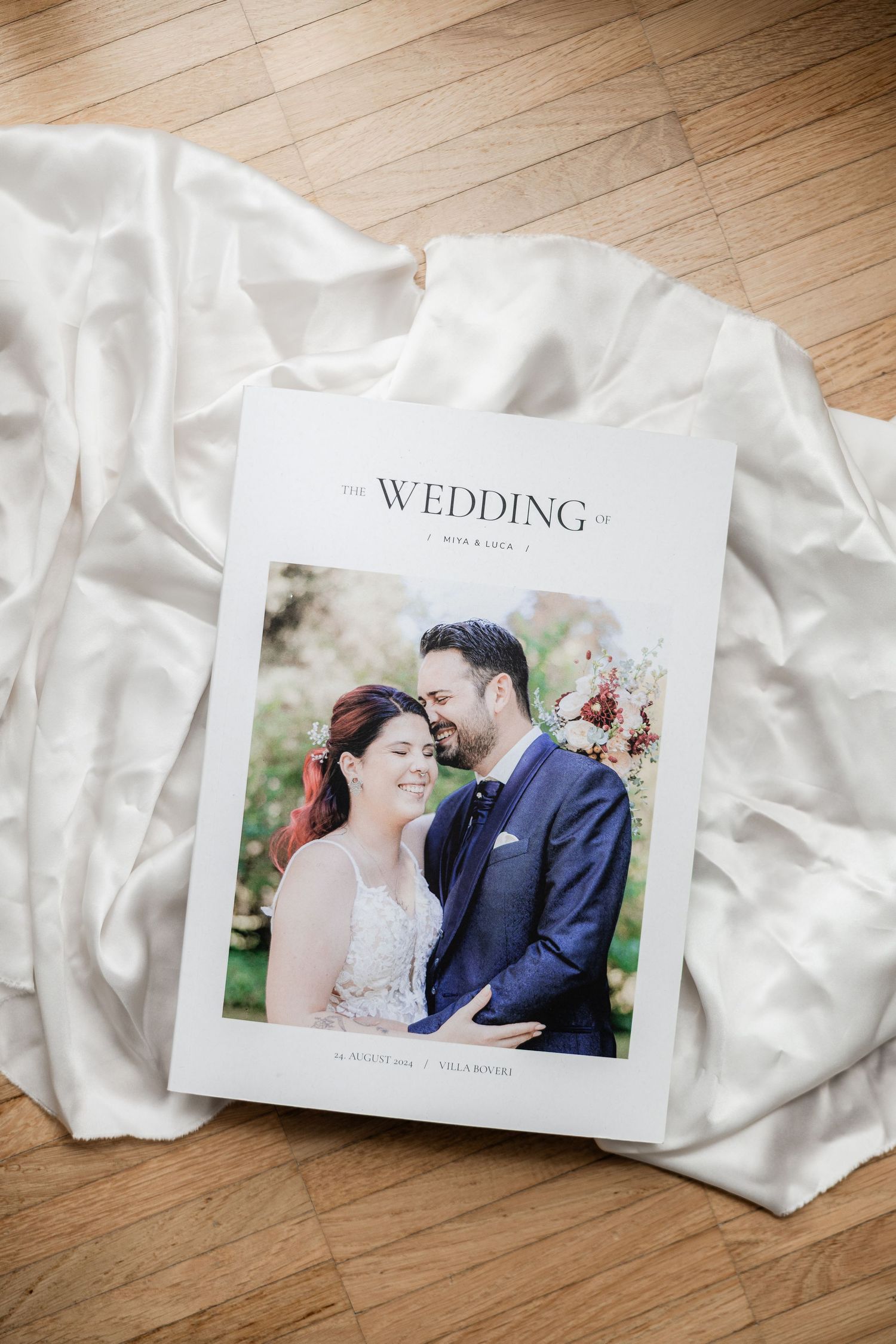 Wedding photo album with white silk fabric on wooden floor displays elegant romantic photography.