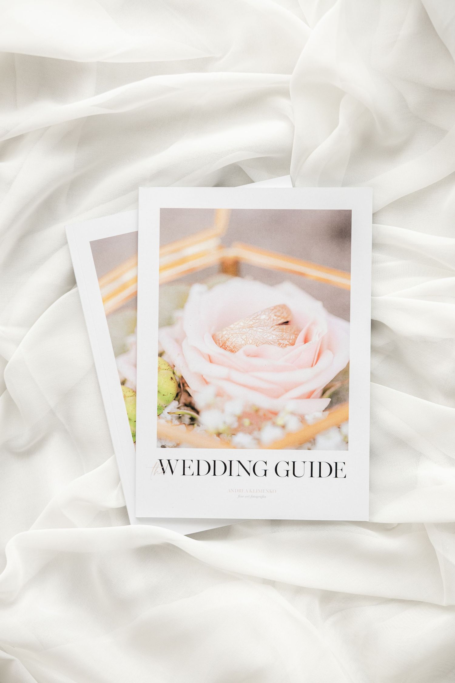 A Wedding Guide booklet featuring a pink rose and gold rings on white silk fabric backdrop.