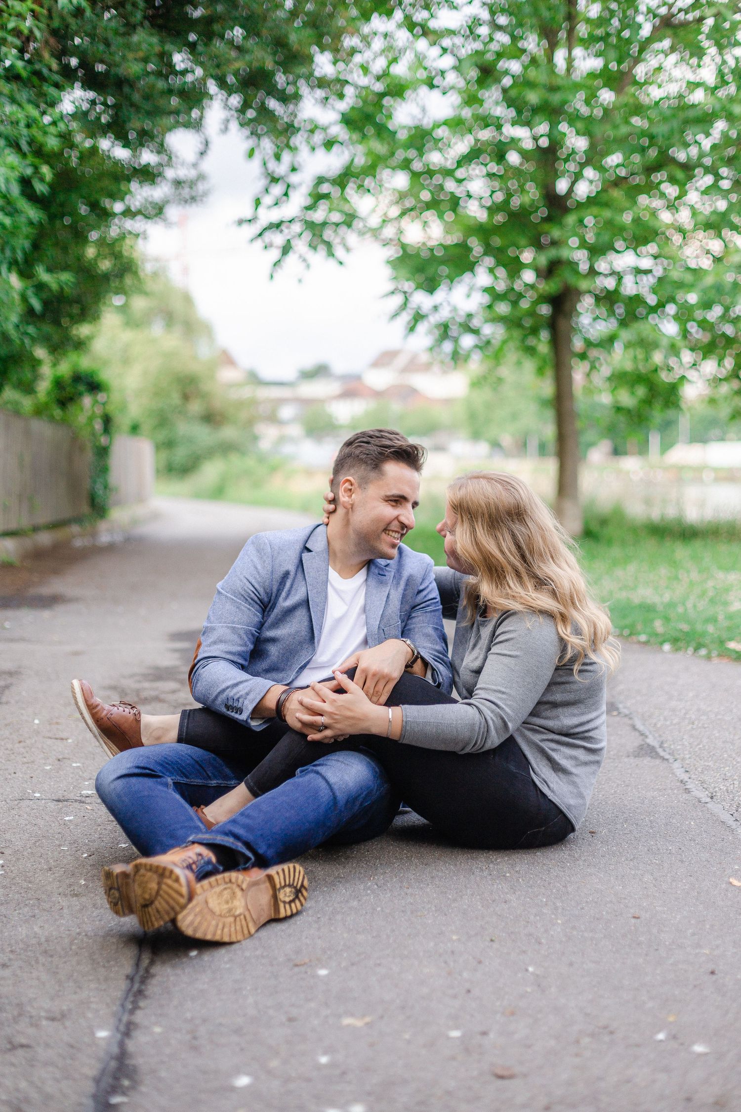 Happy couple sitting together on a path in a lush green park, smiling and enjoying each others company outdoors.