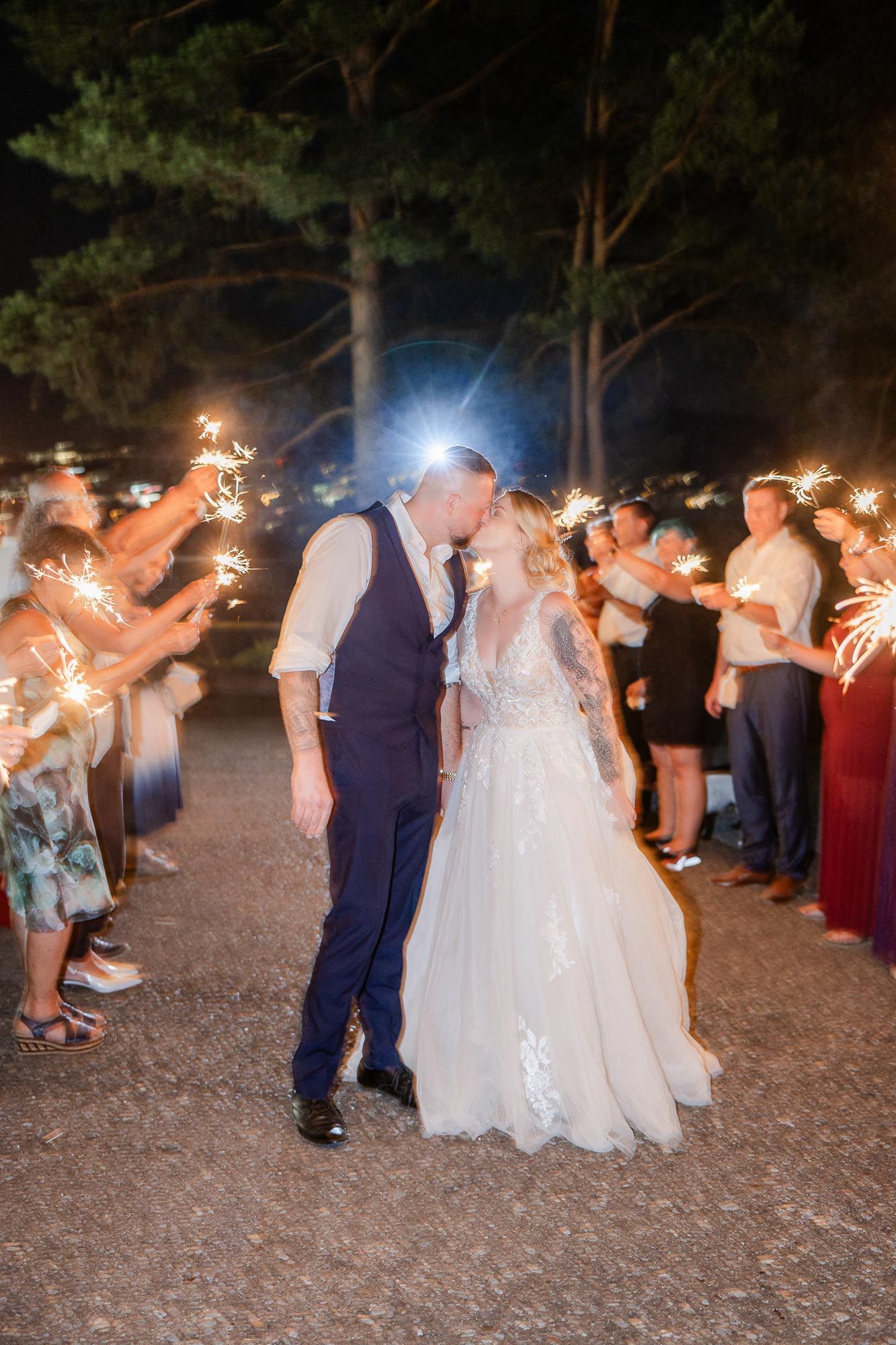 Bride and groom share a kiss during a romantic sparkler exit at their outdoor evening wedding reception.