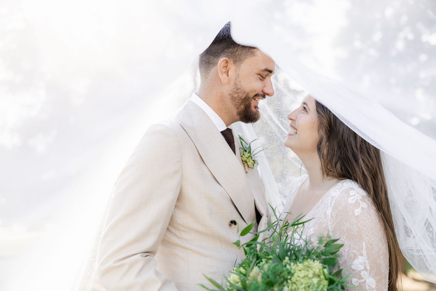 A bride and groom share a joyful moment together outdoors while holding a green floral bouquet. Flims, GR, Switzerland