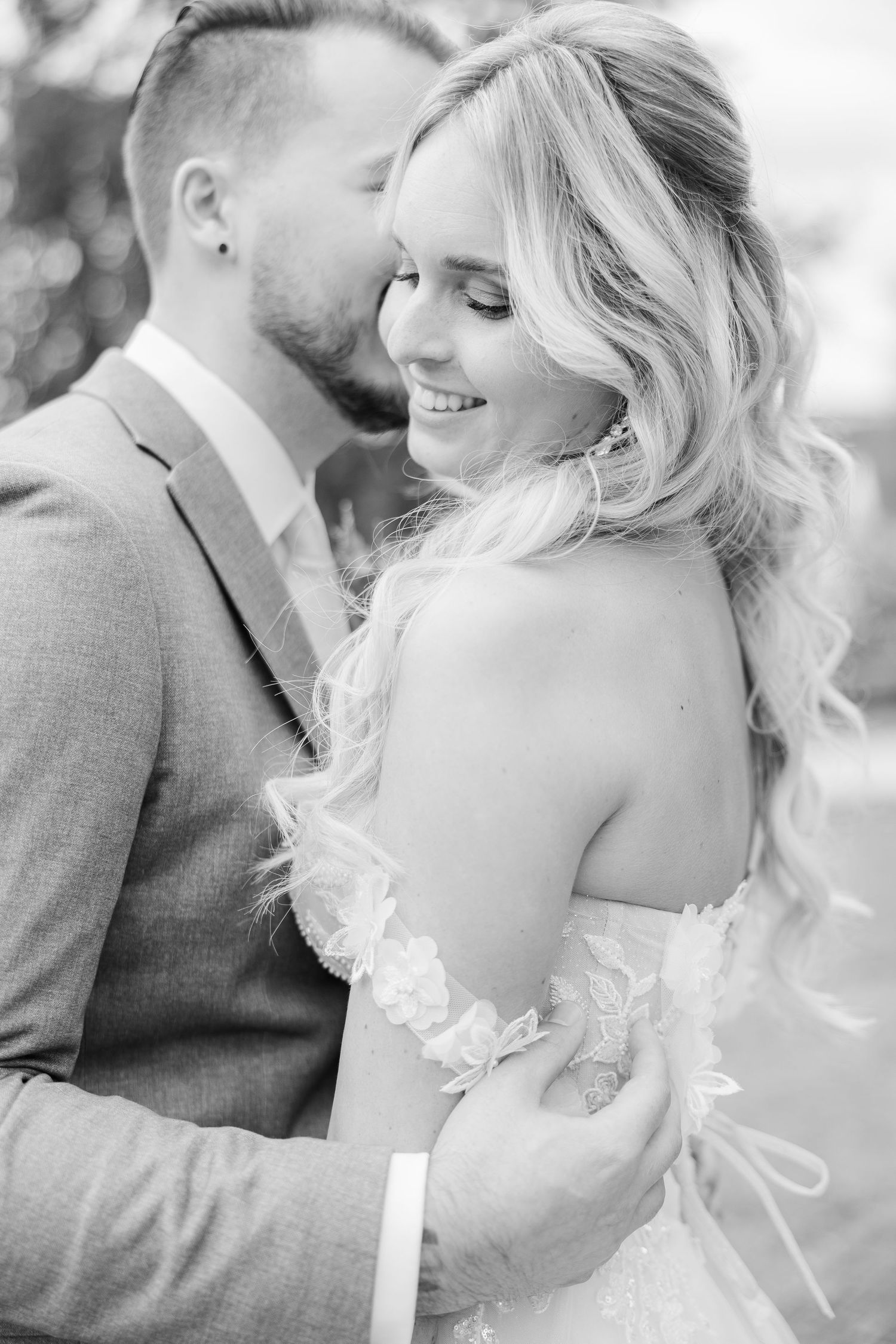 Black and white intimate wedding portrait of a couple embracing outdoors with soft natural lighting.