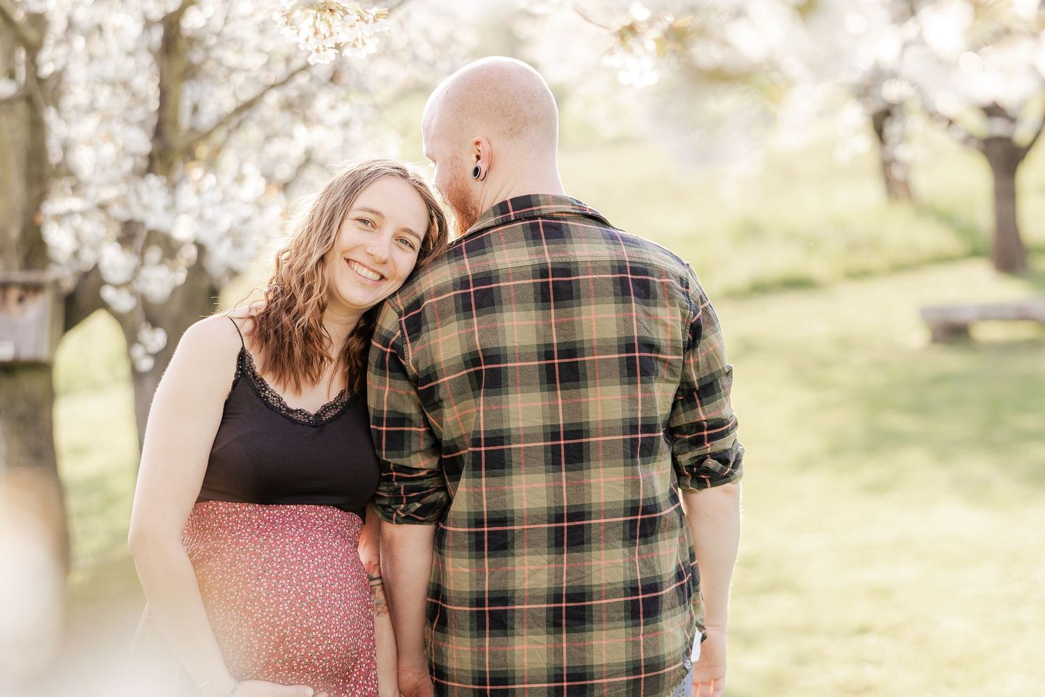 A couple in coordinated outfits sharing tender moments in a sun-drenched outdoor setting during a photo session.