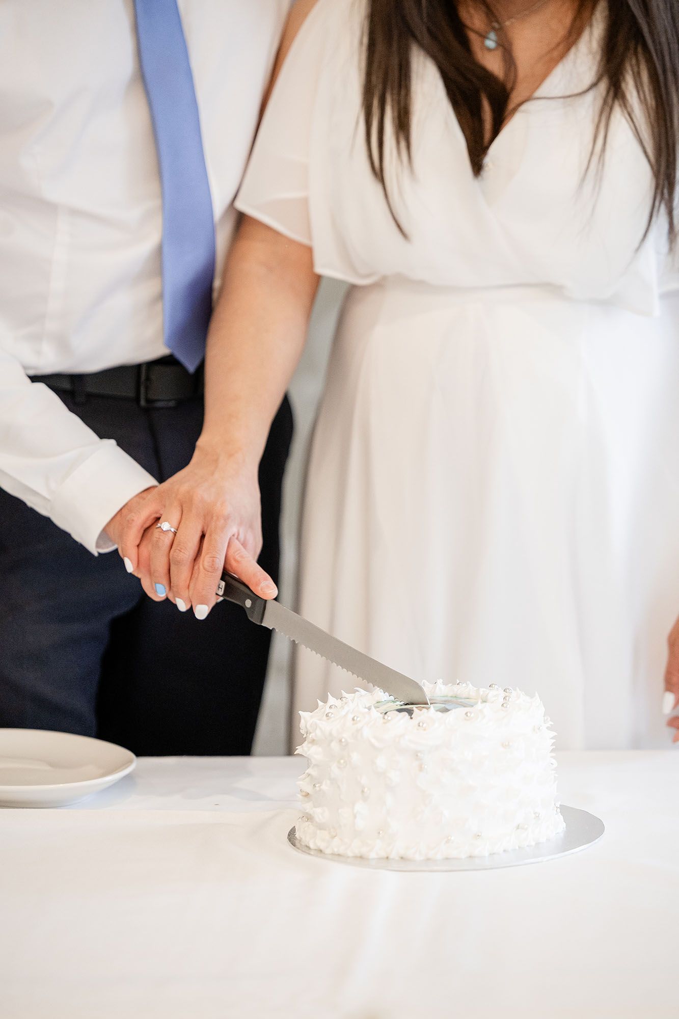 Bride and groom cutting a white coconut wedding cake together at a reception table.