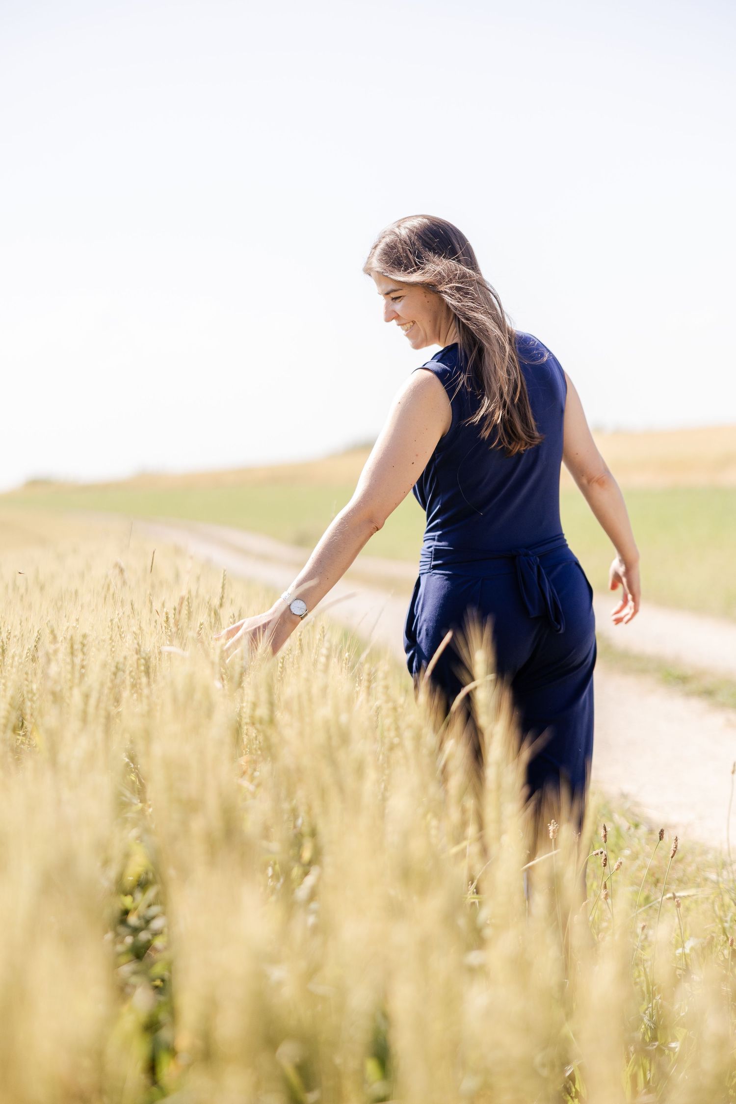 A woman in a navy dress walks through a golden wheat field on a sunny summer day.